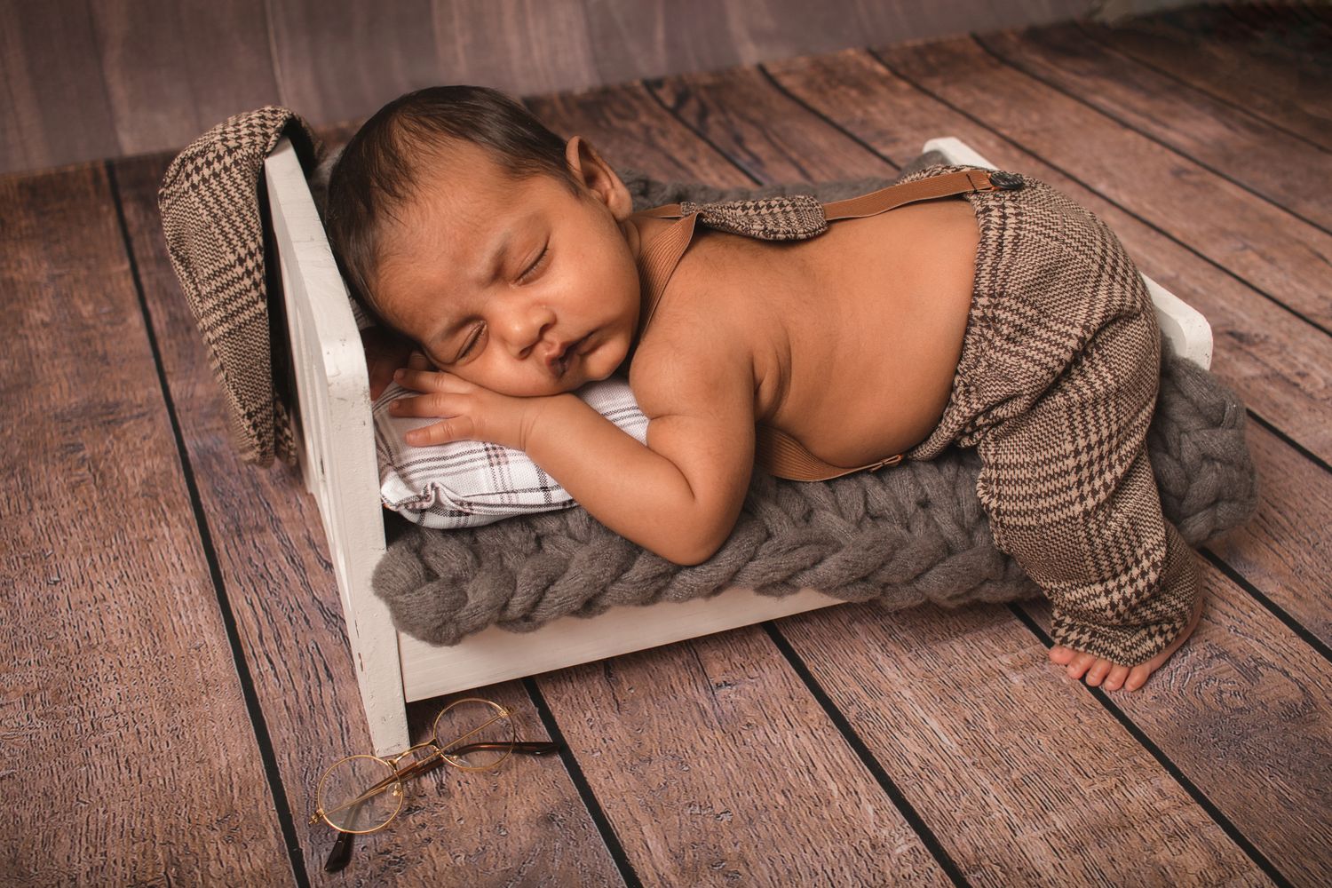 Newborn baby sleeping peacefully on wooden backdrop with brown wrap.
