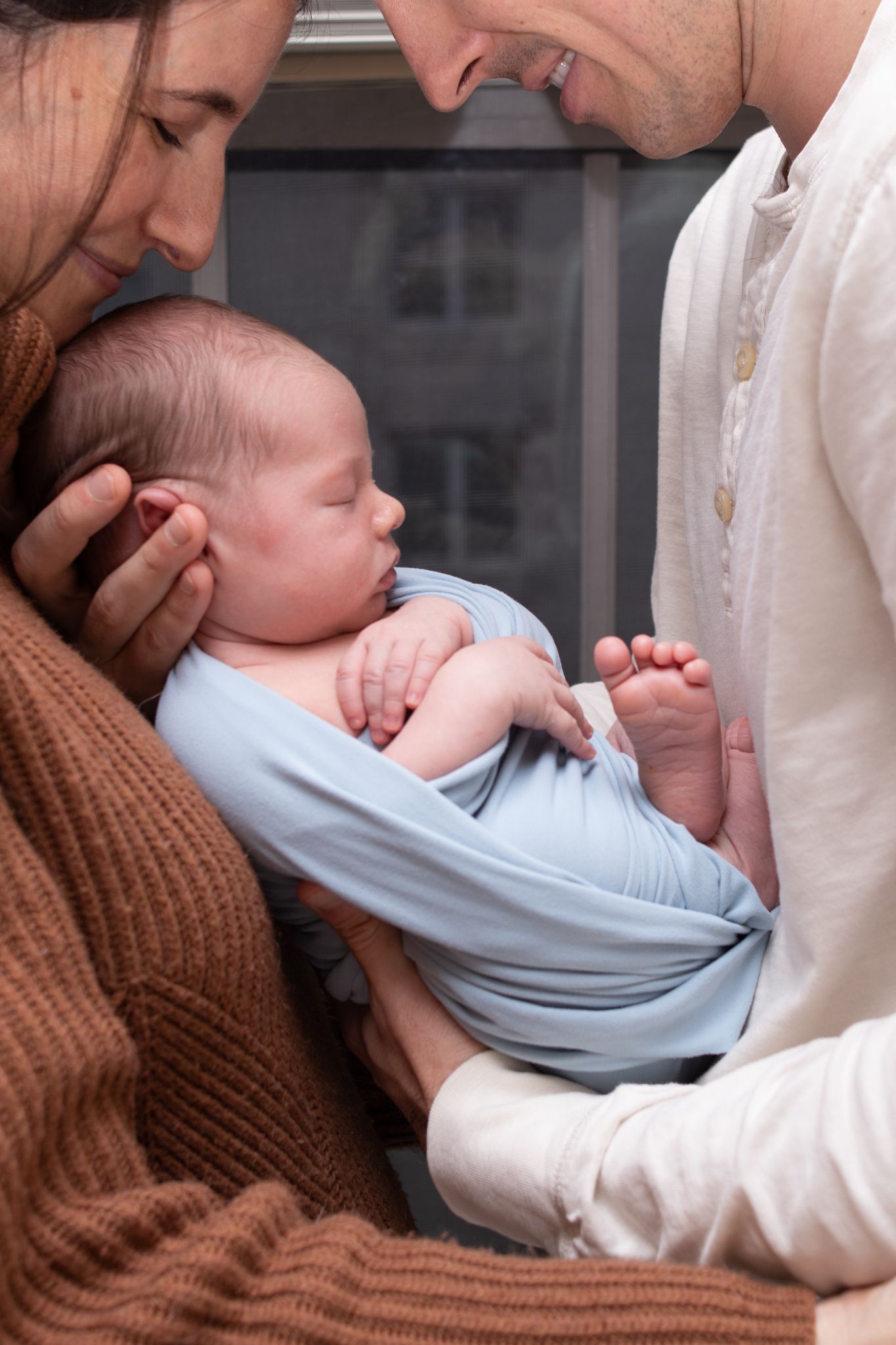 Intimate moment with newborn baby wrapped in light blue swaddle.