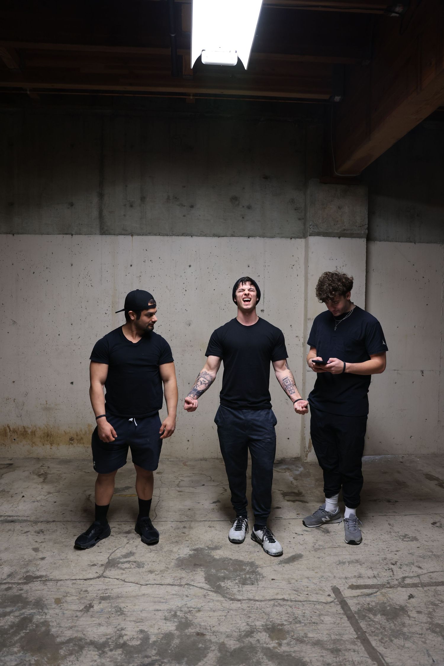 Three men in black clothing having animated conversation against concrete wall.