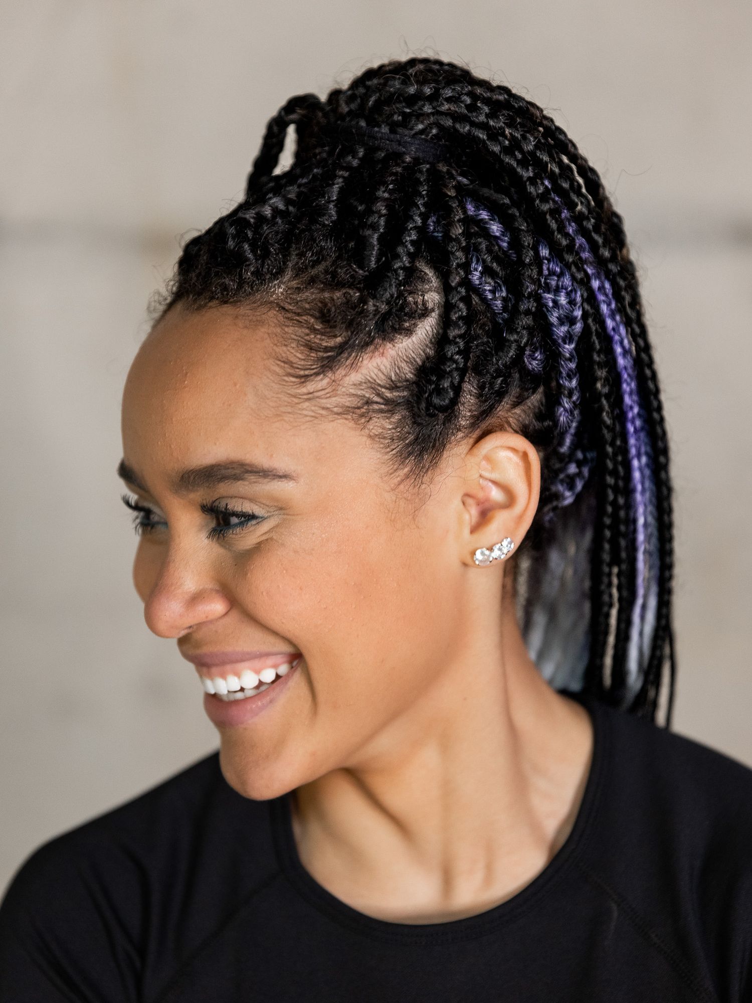 Woman with intricate purple-accented braided hairstyle wearing black top.