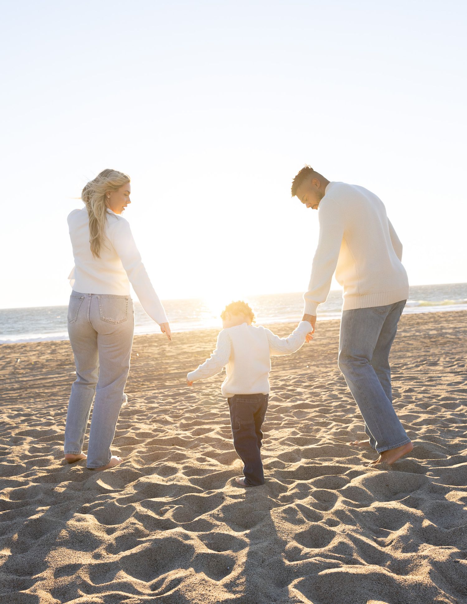 Family holding hands and walking together on a sandy beach during golden sunset.