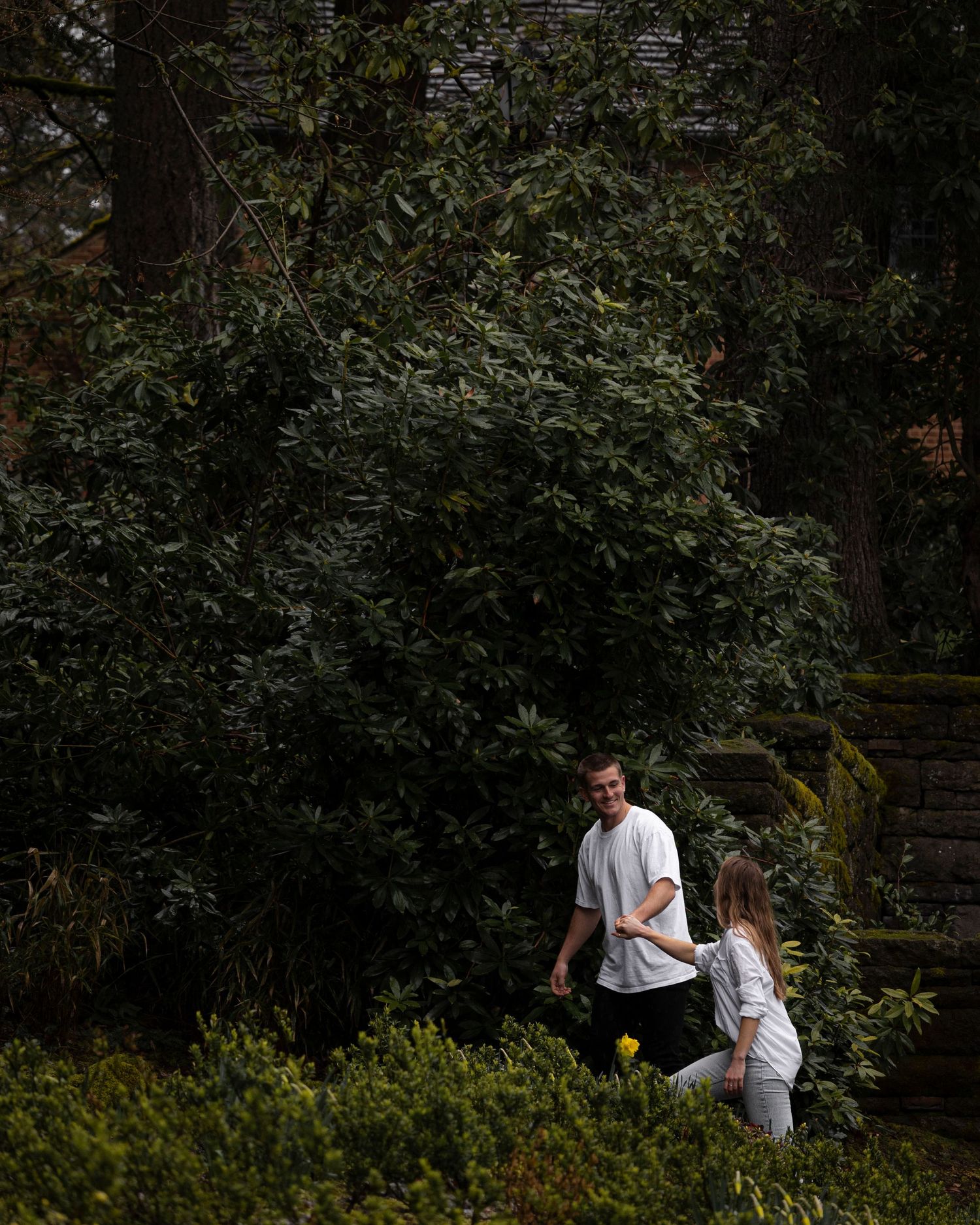 Two people in matching white outfits walk up moss-covered stone steps in a lush garden setting.