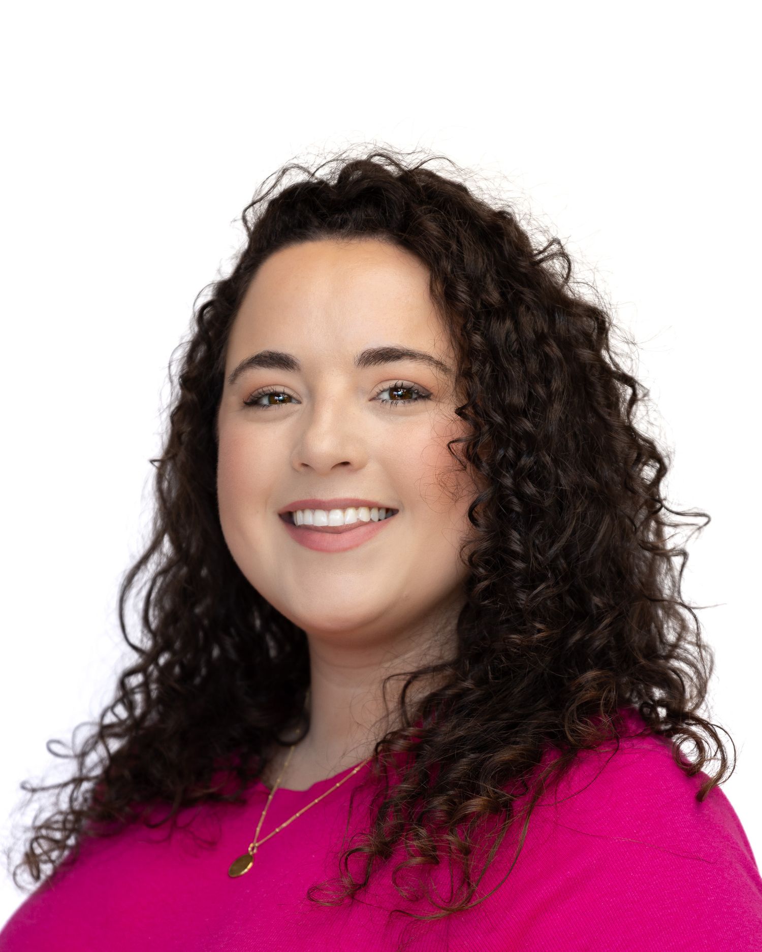 Professional headshot of someone wearing a bright pink sweater and necklace with natural curly dark hair and warm smile.