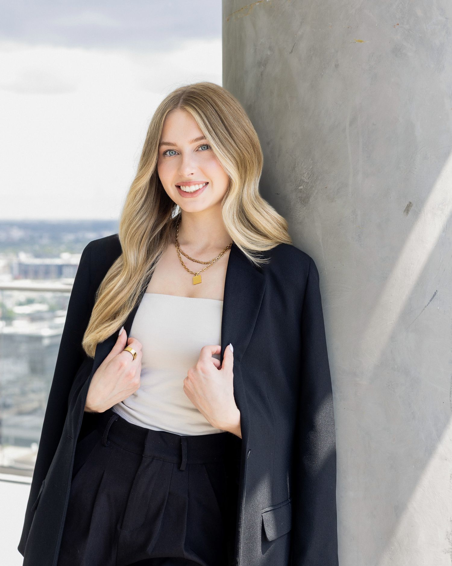 Professional portrait of someone in business attire smiling against a modern architectural background.