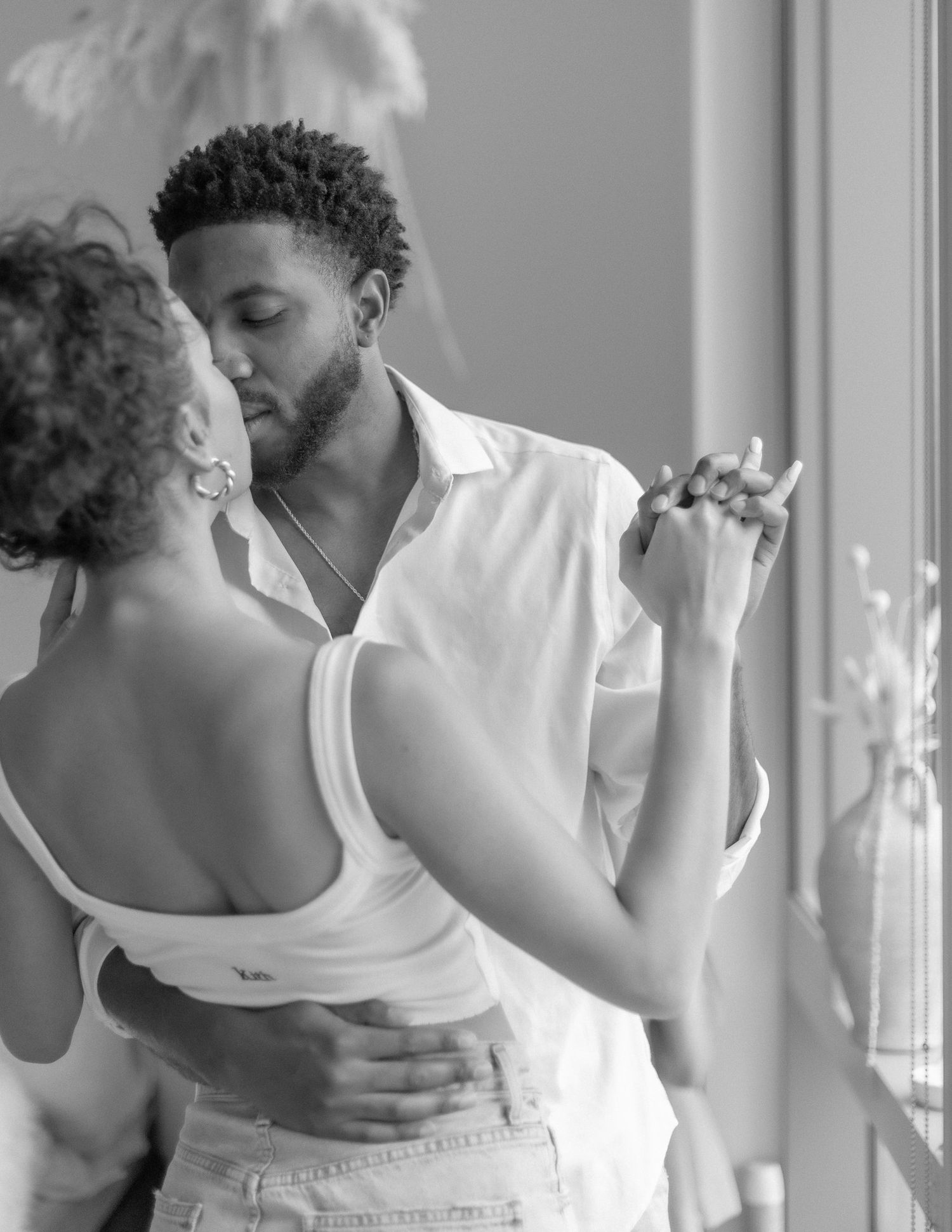 Romantic black and white photo of a couple dancing intimately by window light.