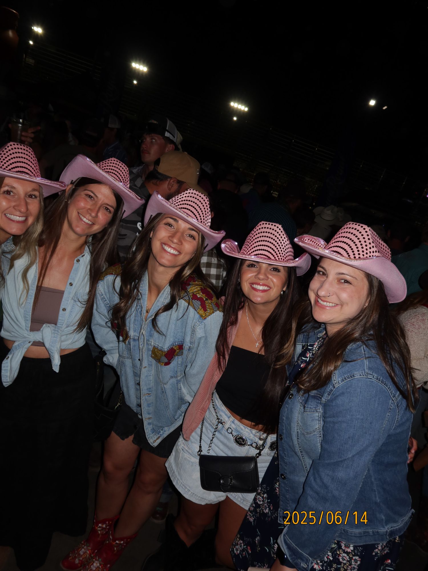 A group of friends wearing striped hats and denim jackets pose together at a nighttime event.