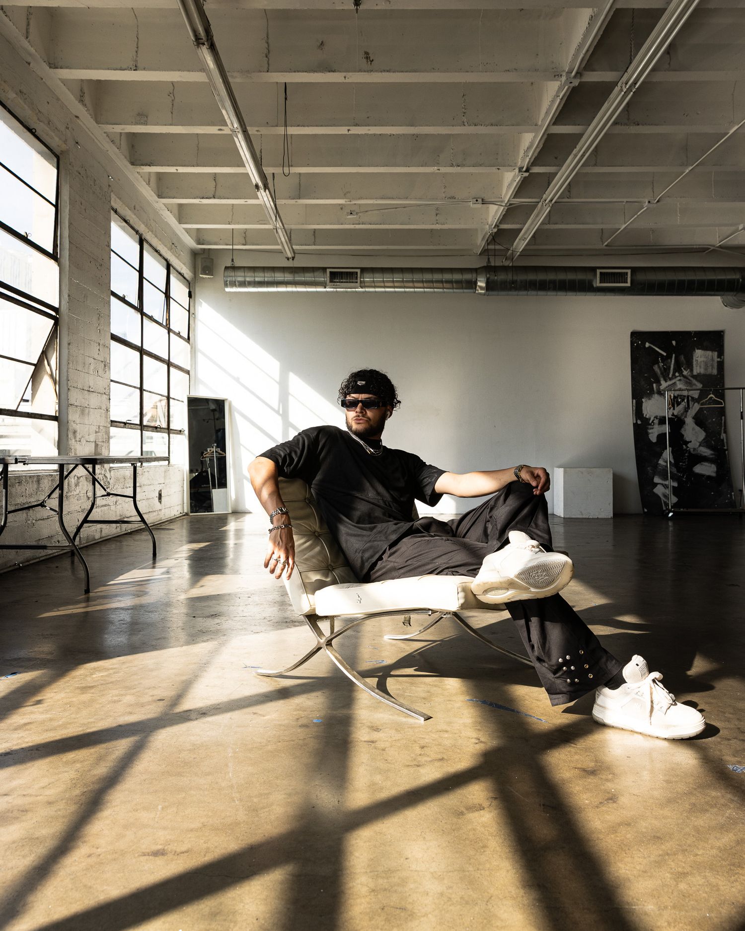 Person relaxing in modern loft space on white lounge chair with sunlight casting dramatic shadows through windows.