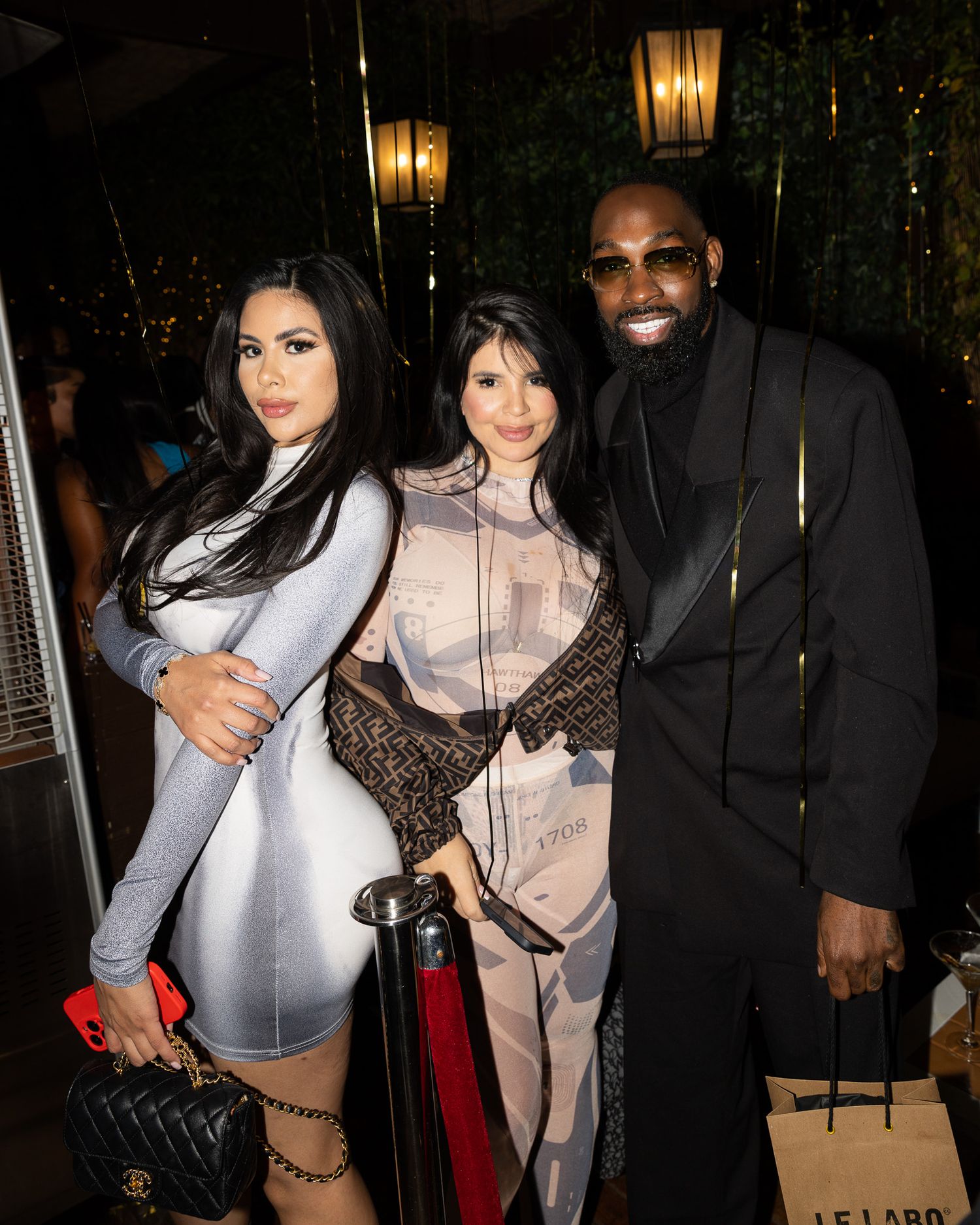 Three people pose together at a nighttime event with glowing lanterns in the background.