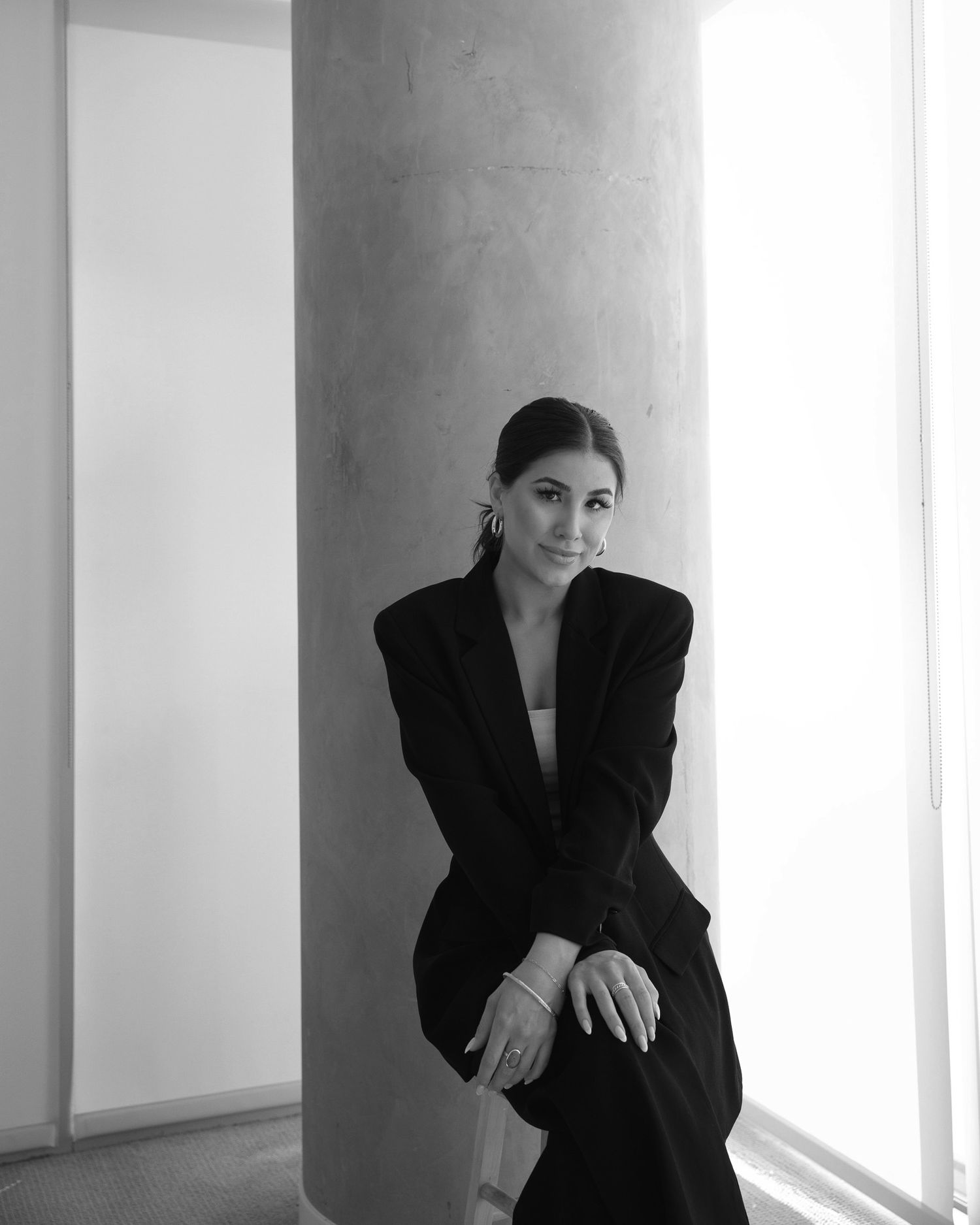 Dramatic black and white portrait of someone in an oversized blazer posing against a minimalist white wall.