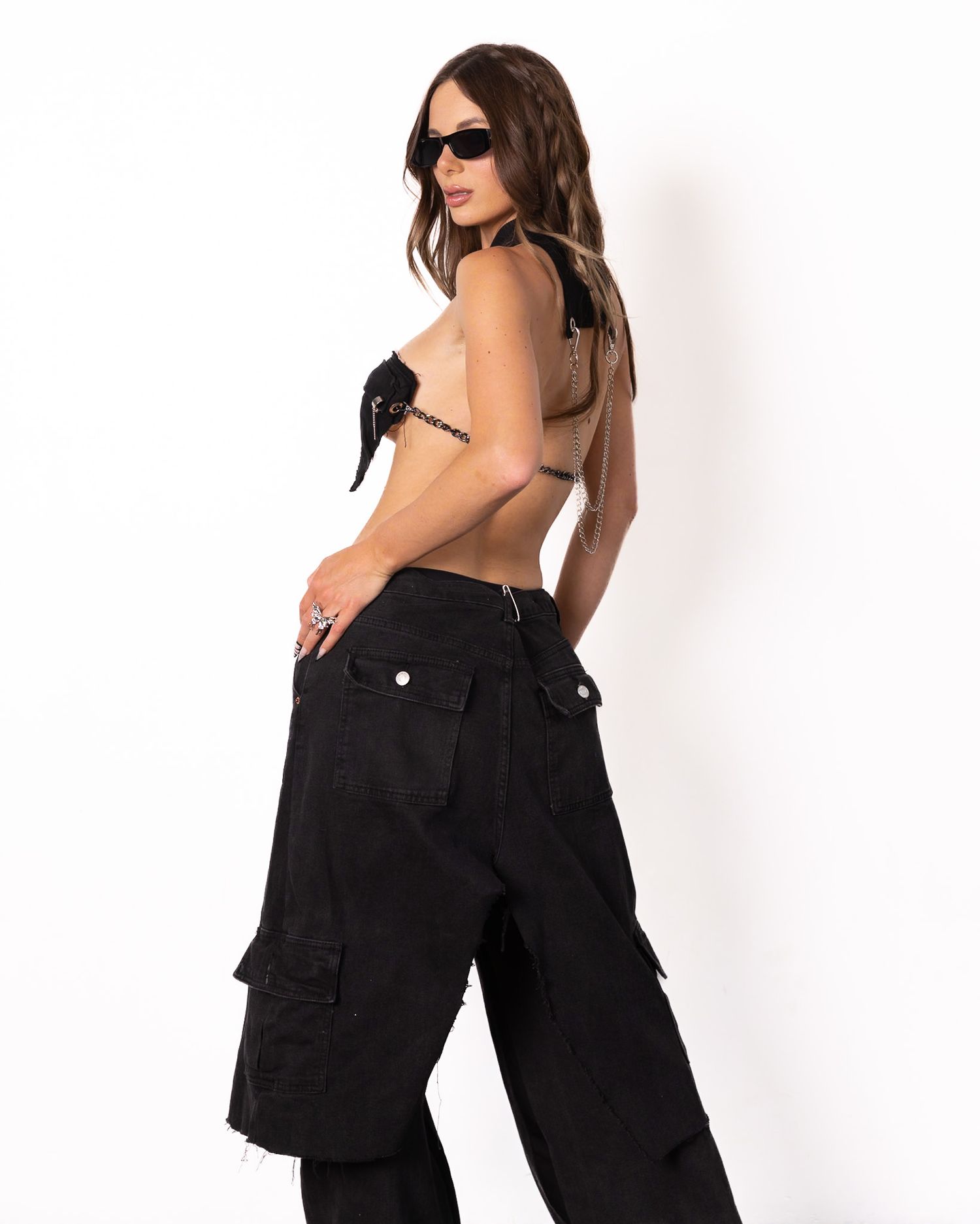 Fashion model in black cargo pants and crop top poses against white background.