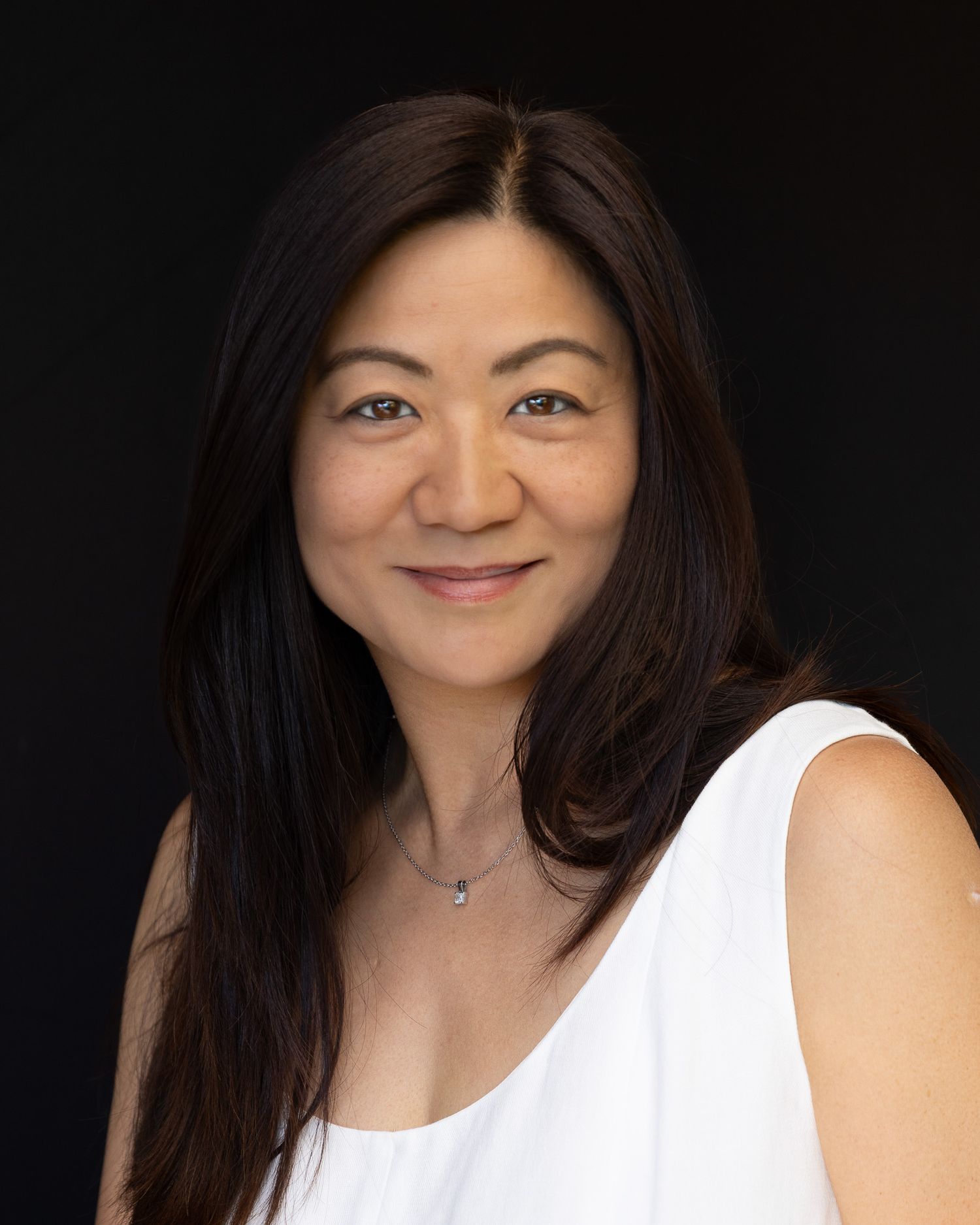 Professional headshot portrait of someone in a white sleeveless top against a dark background.