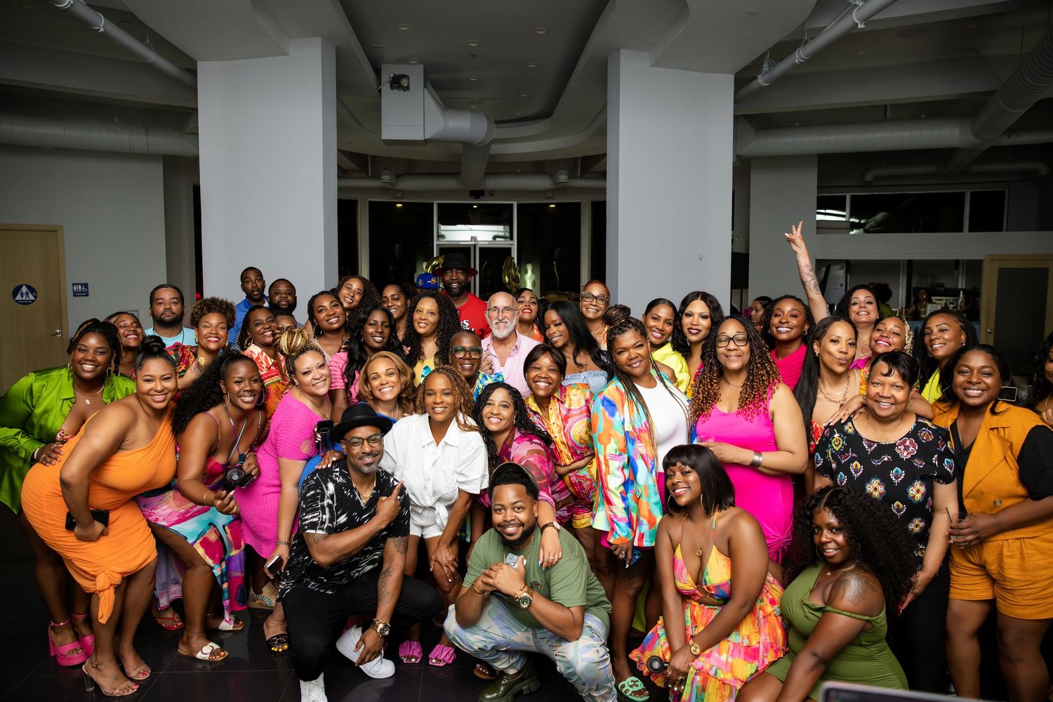 Large group poses together at a celebratory event wearing vibrant summer attire.