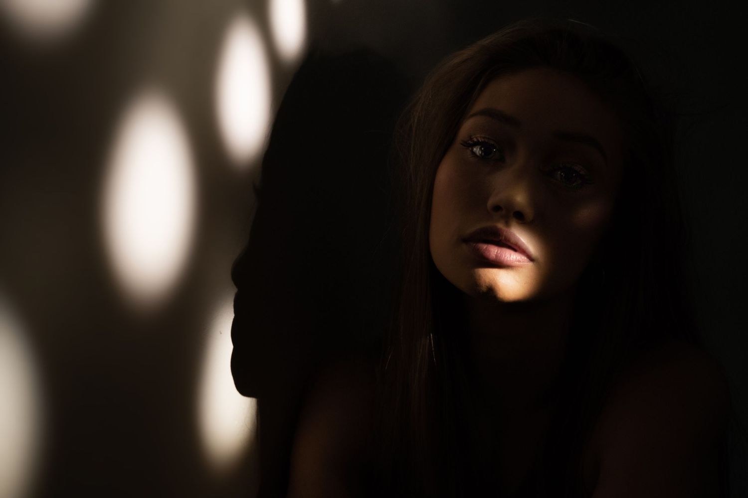 Dramatic portrait in dark lighting with circular light spots creating an atmospheric shadow effect.