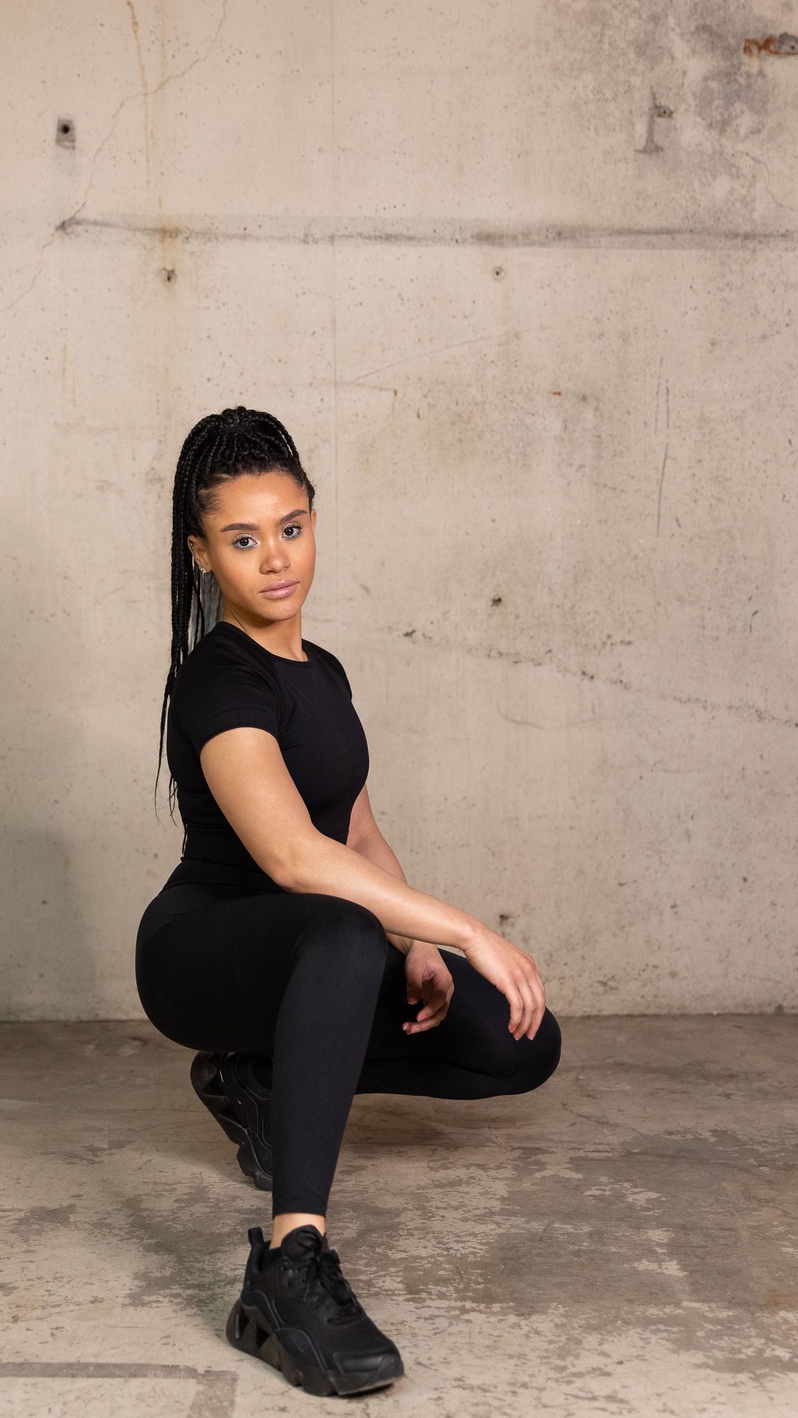 Athlete in all-black activewear sitting on concrete floor in urban setting.