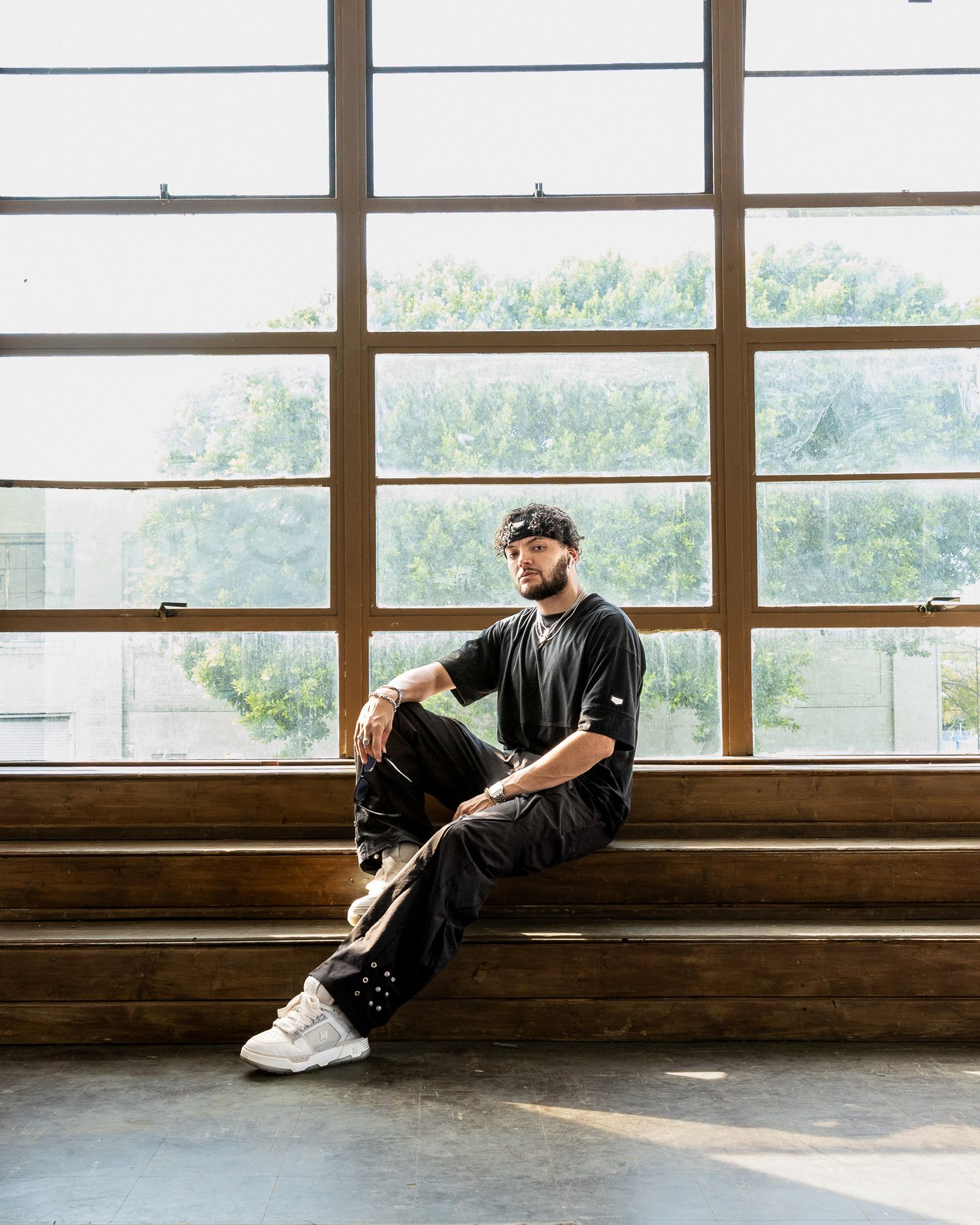 Person in dark clothing sits on wooden steps near large windows in natural light filled space.