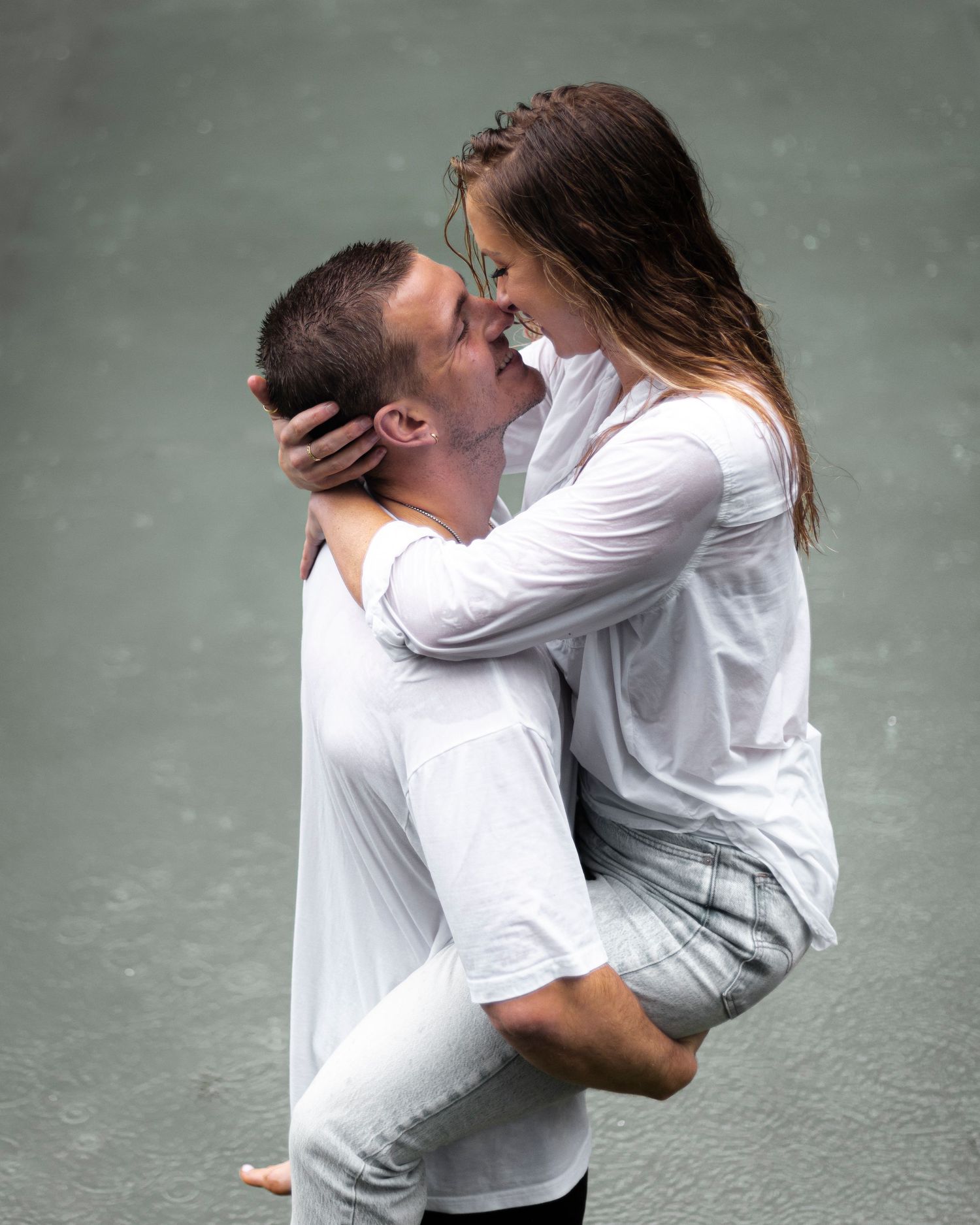 Two people dressed in white embrace intimately while standing together outdoors.