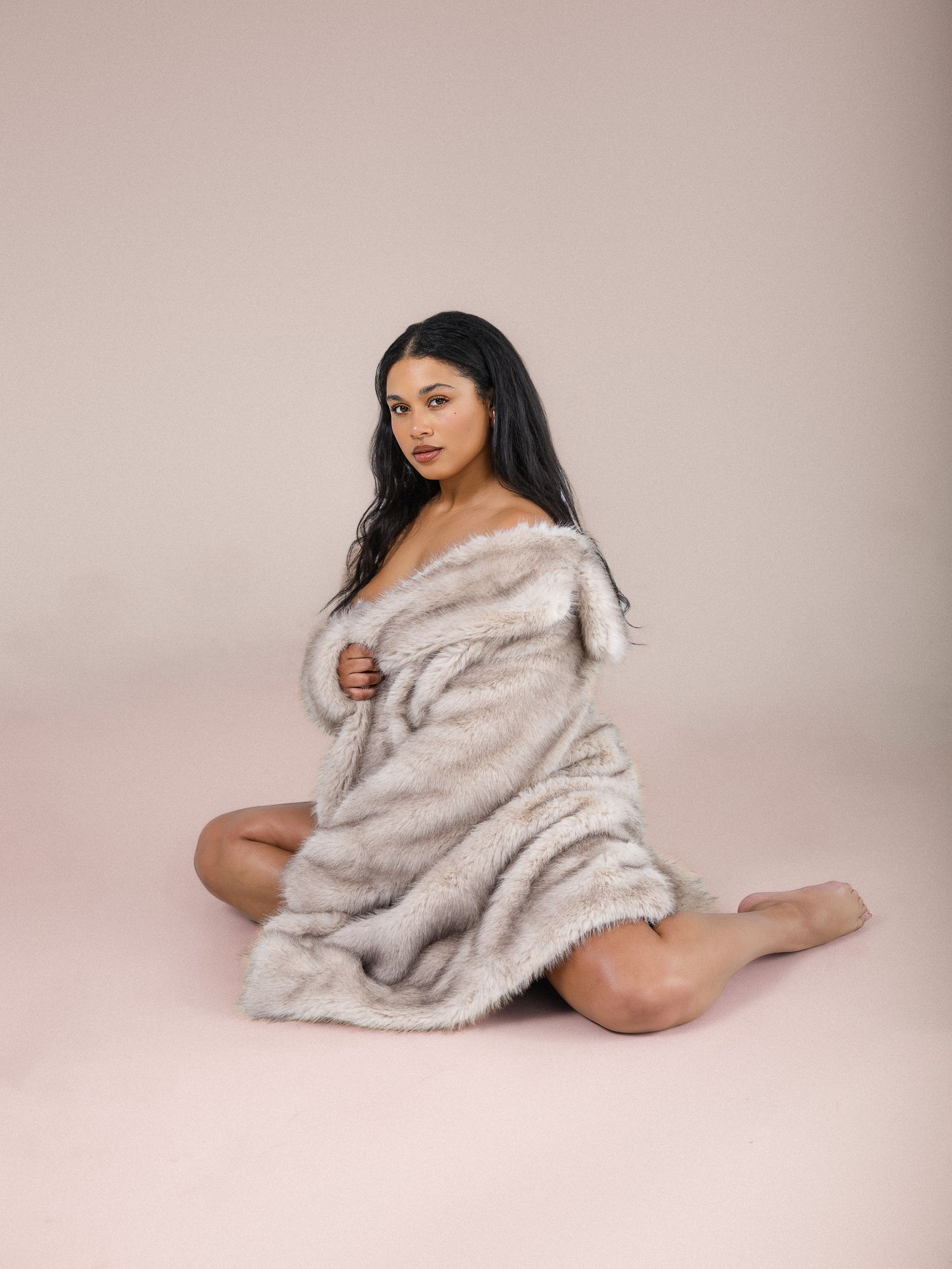 Woman wearing luxurious grey faux fur coat poses elegantly on pink studio background.