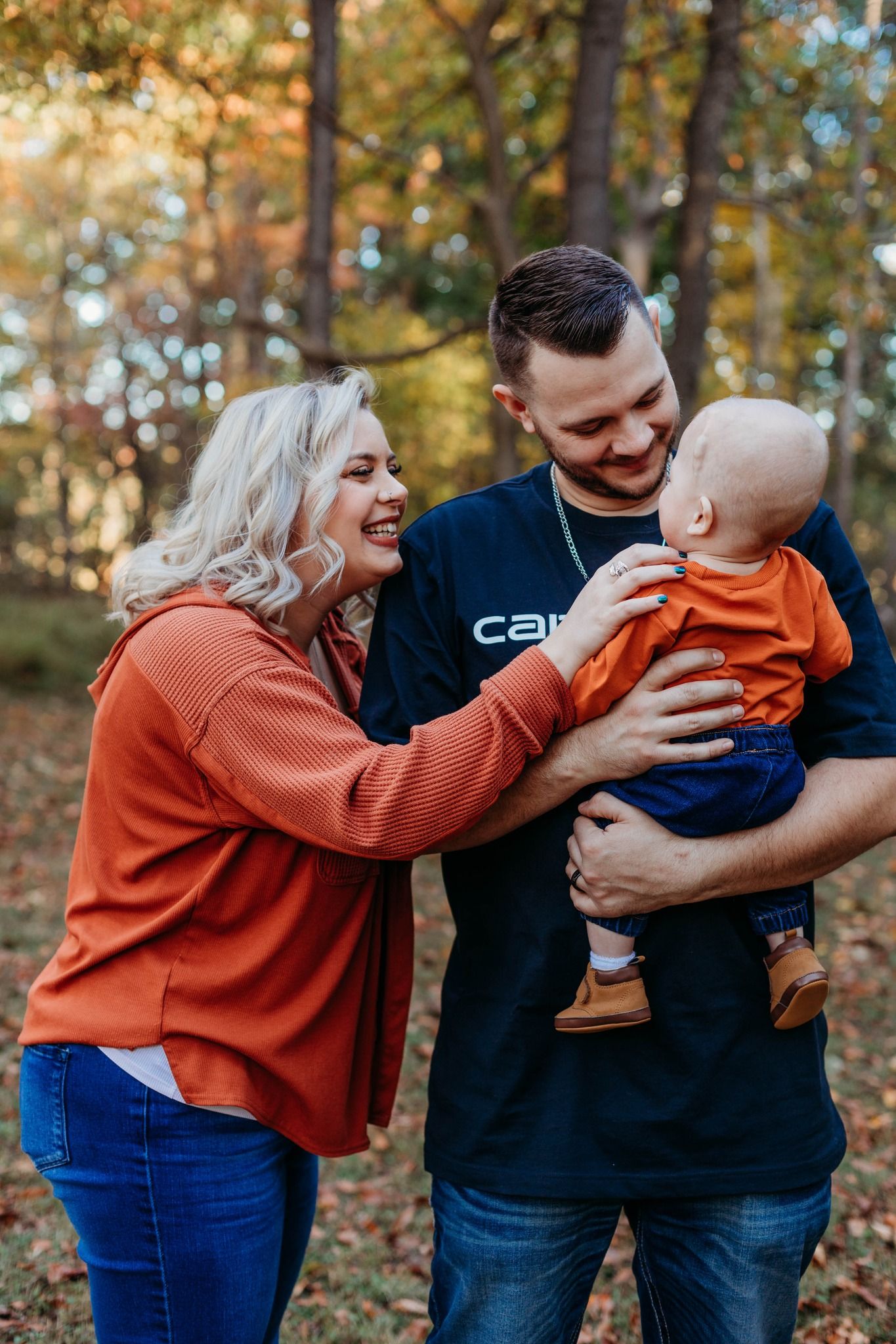Family wearing orange and navy share playful moments in an autumn forest setting.