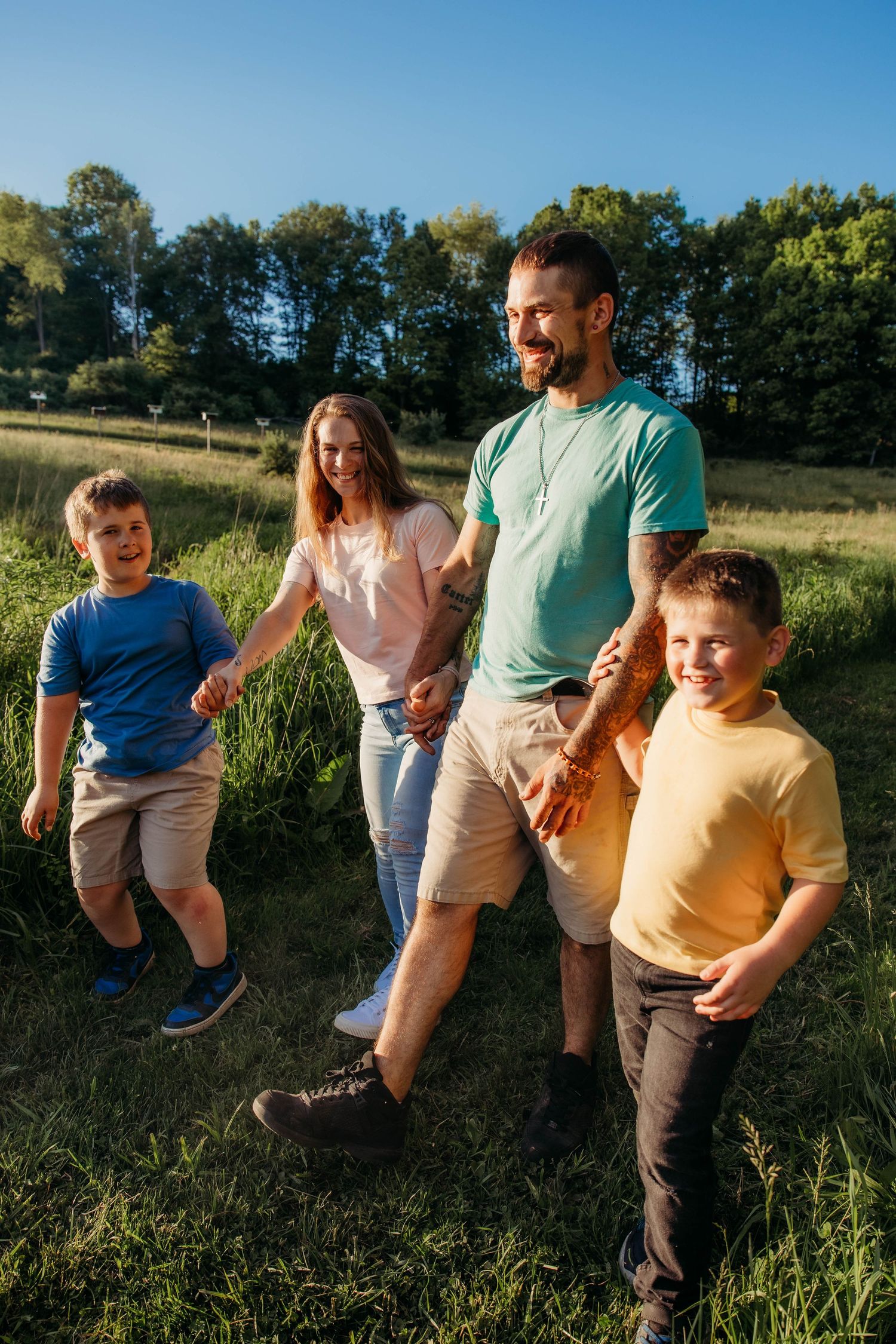 Happy family of four enjoying a sunny day outdoors in a green meadow with trees in the background.