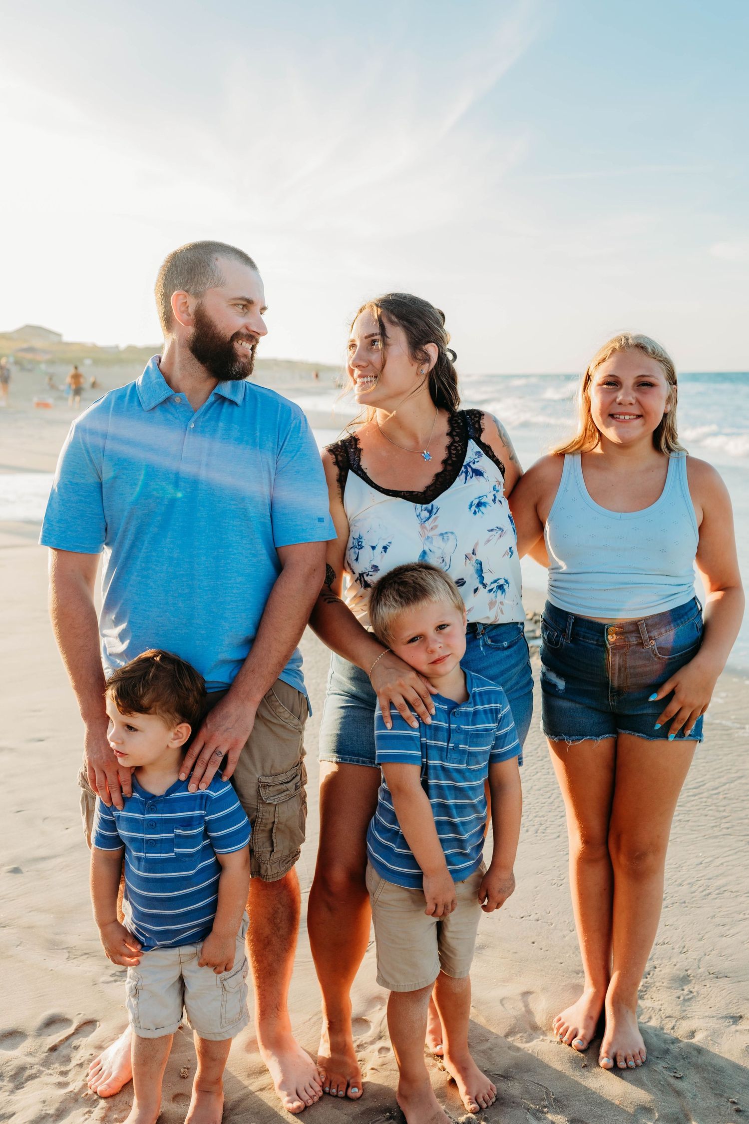 Casual family group wearing coordinated blue and denim outfits posing on a sunny beach.