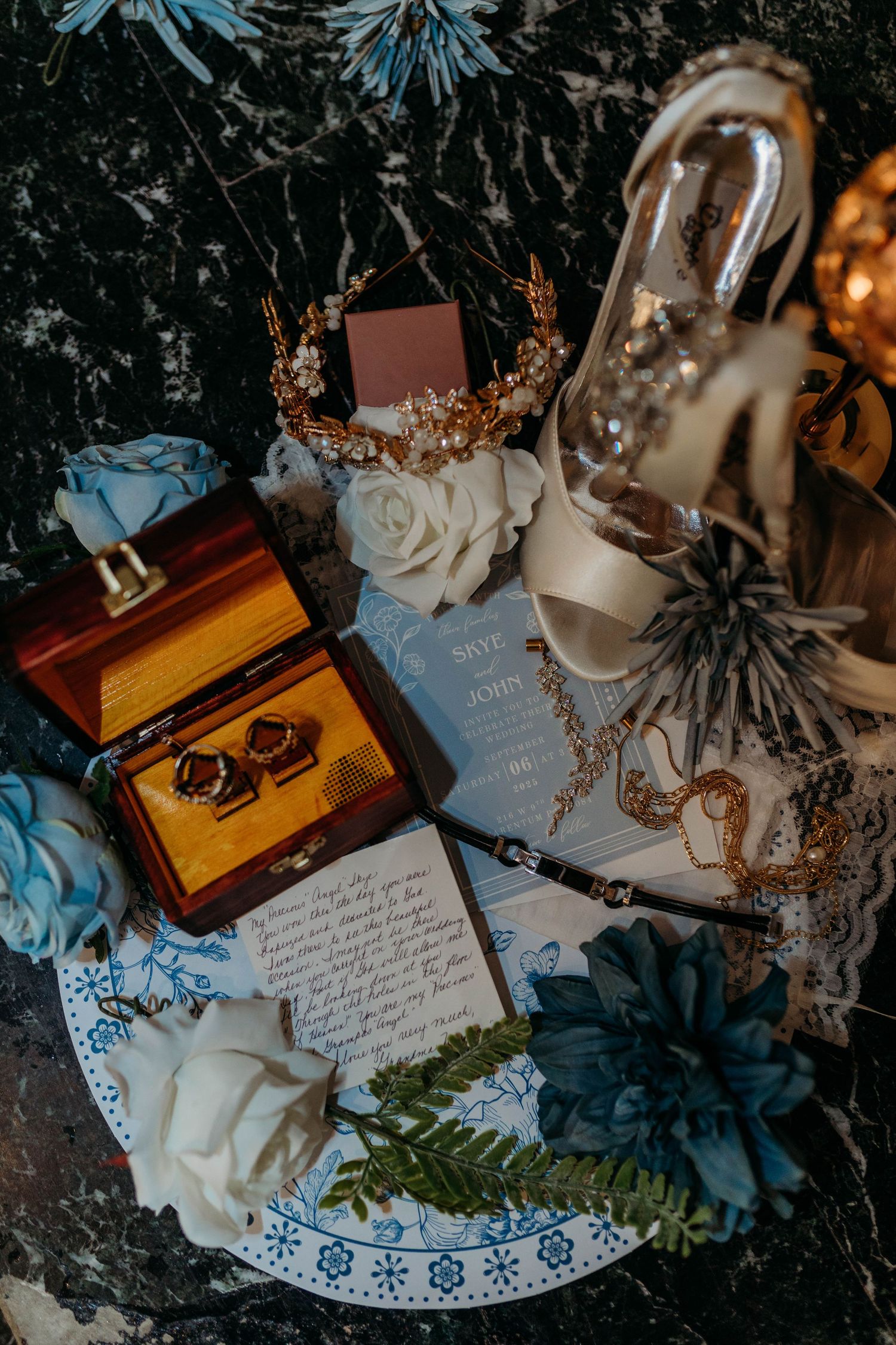 Wedding details including handwritten notes, jewelry, and decorative elements arranged on a dark surface.