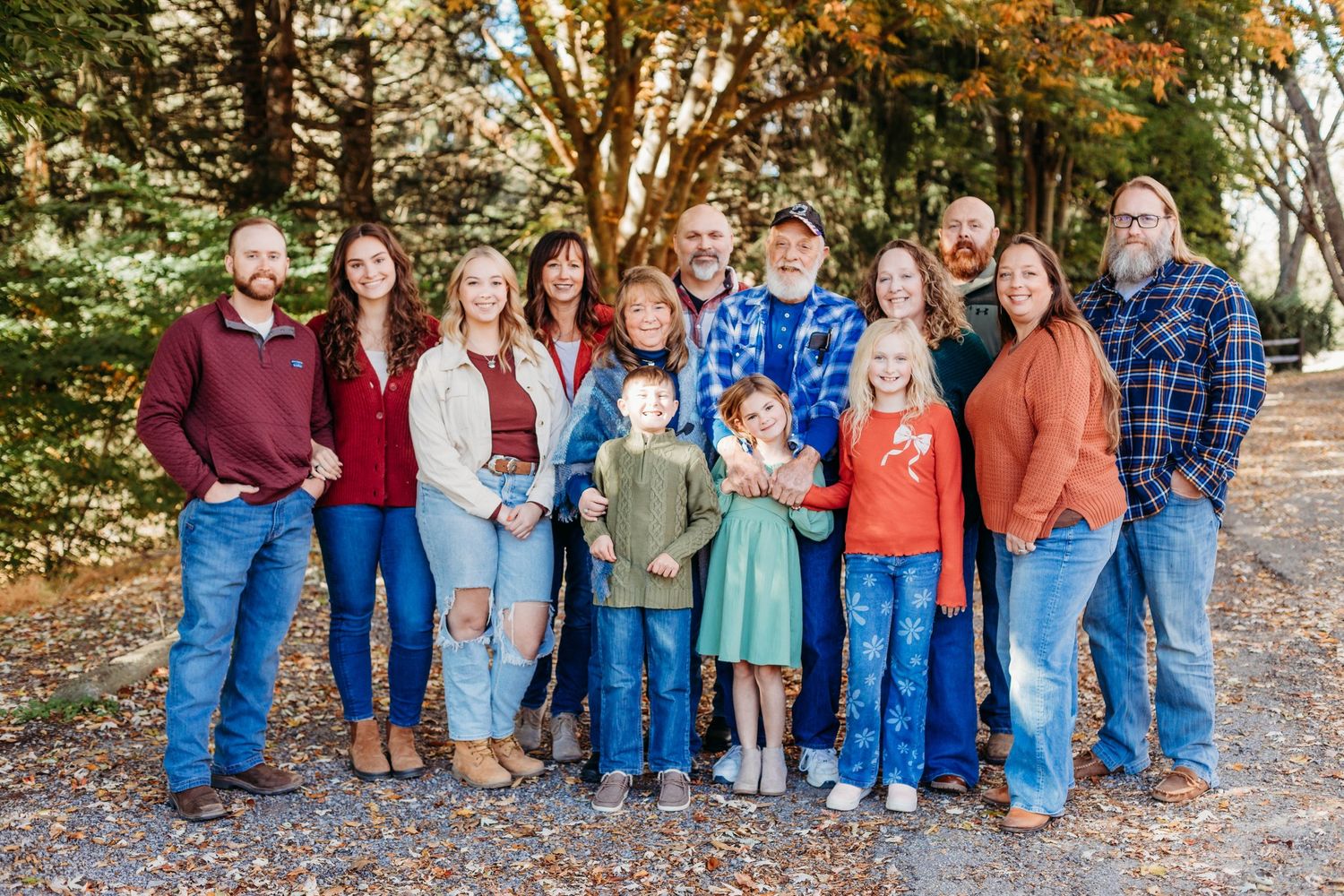 Extended family group portrait outdoors with fall foliage in background.