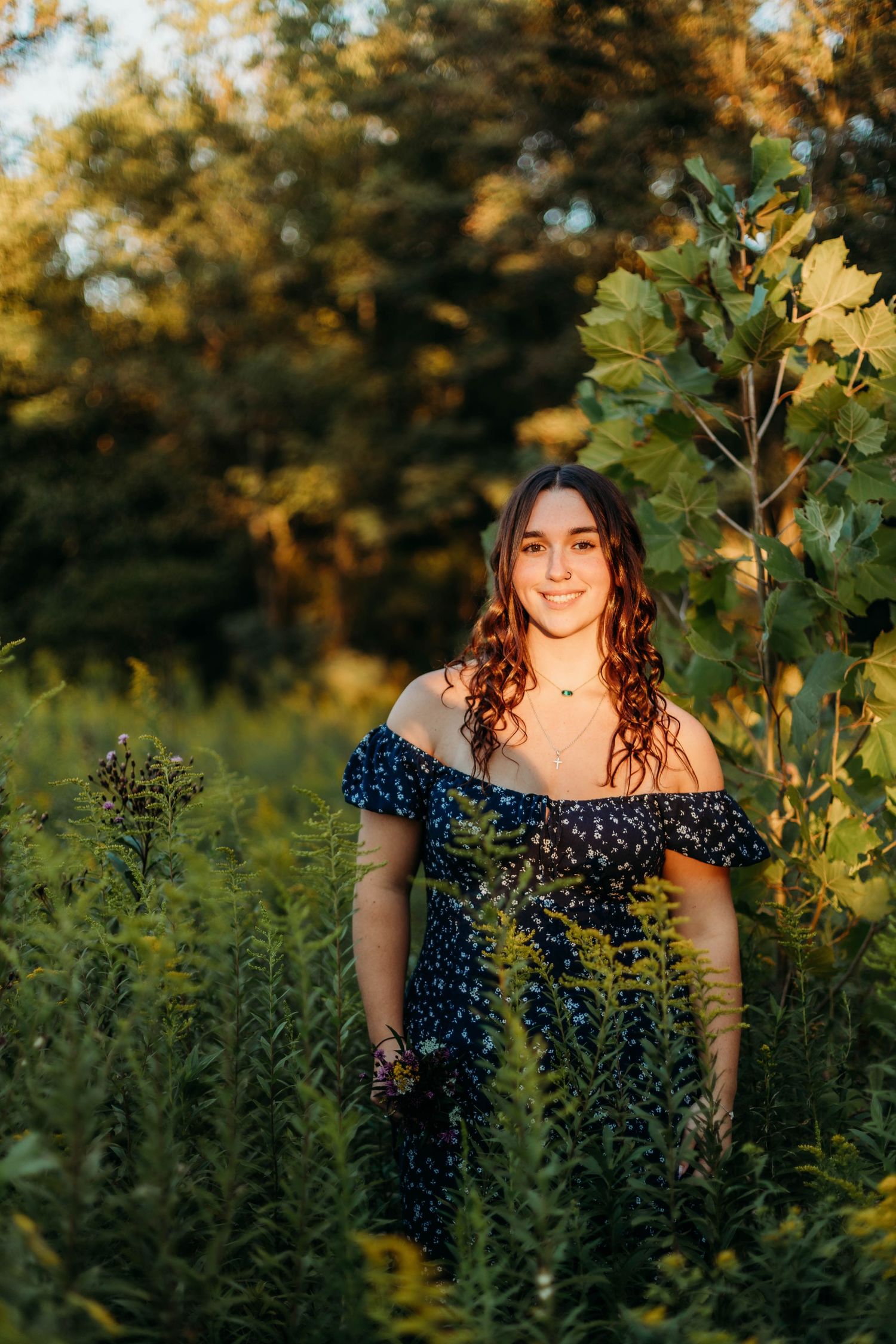 A woman in a floral dress poses in a garden during golden hour sunset.