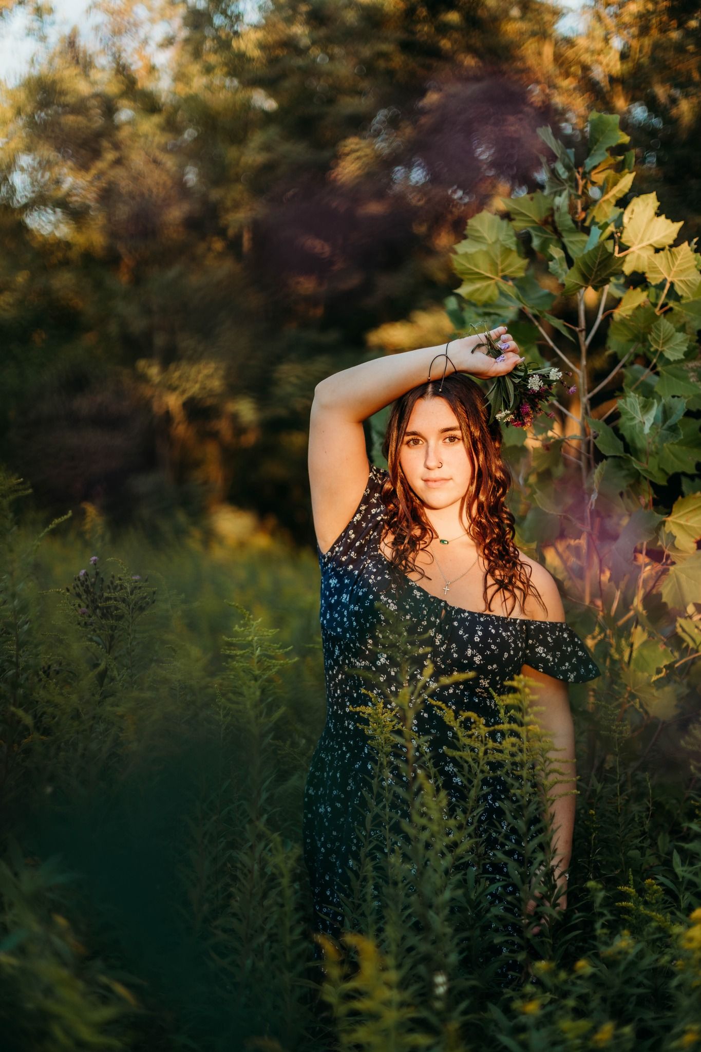 Woman in floral dress poses among foliage at golden hour.