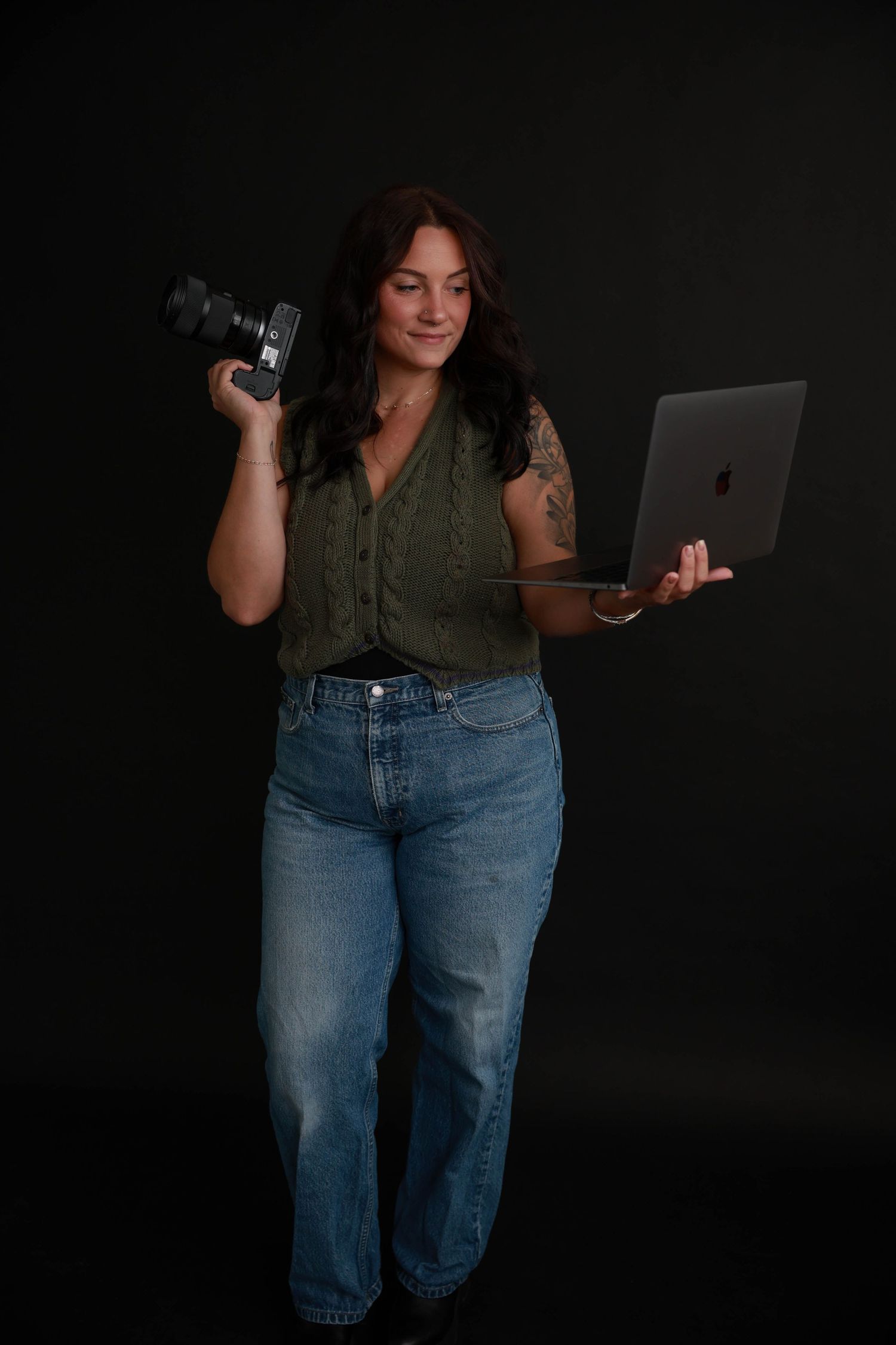 Creative self-portrait of photographer holding camera and laptop in studio setting.