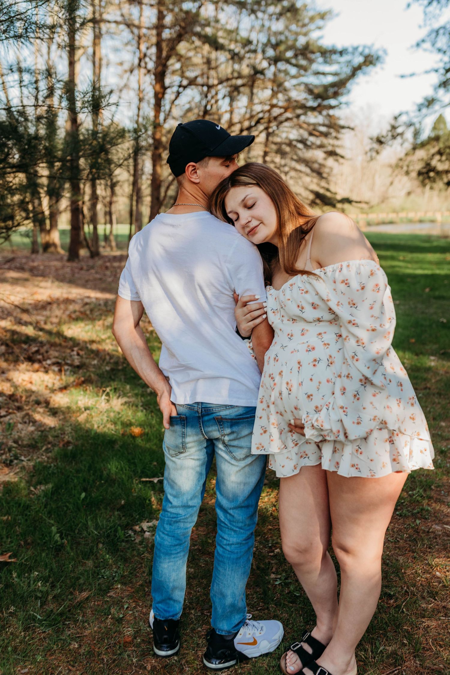 Romantic couple photoshoot in casual outfits against natural forest backdrop.