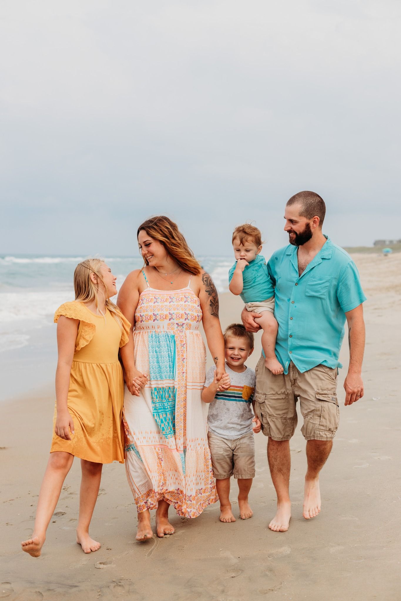 Family walking together on a sandy beach wearing coordinated turquoise and peach colored outfits.