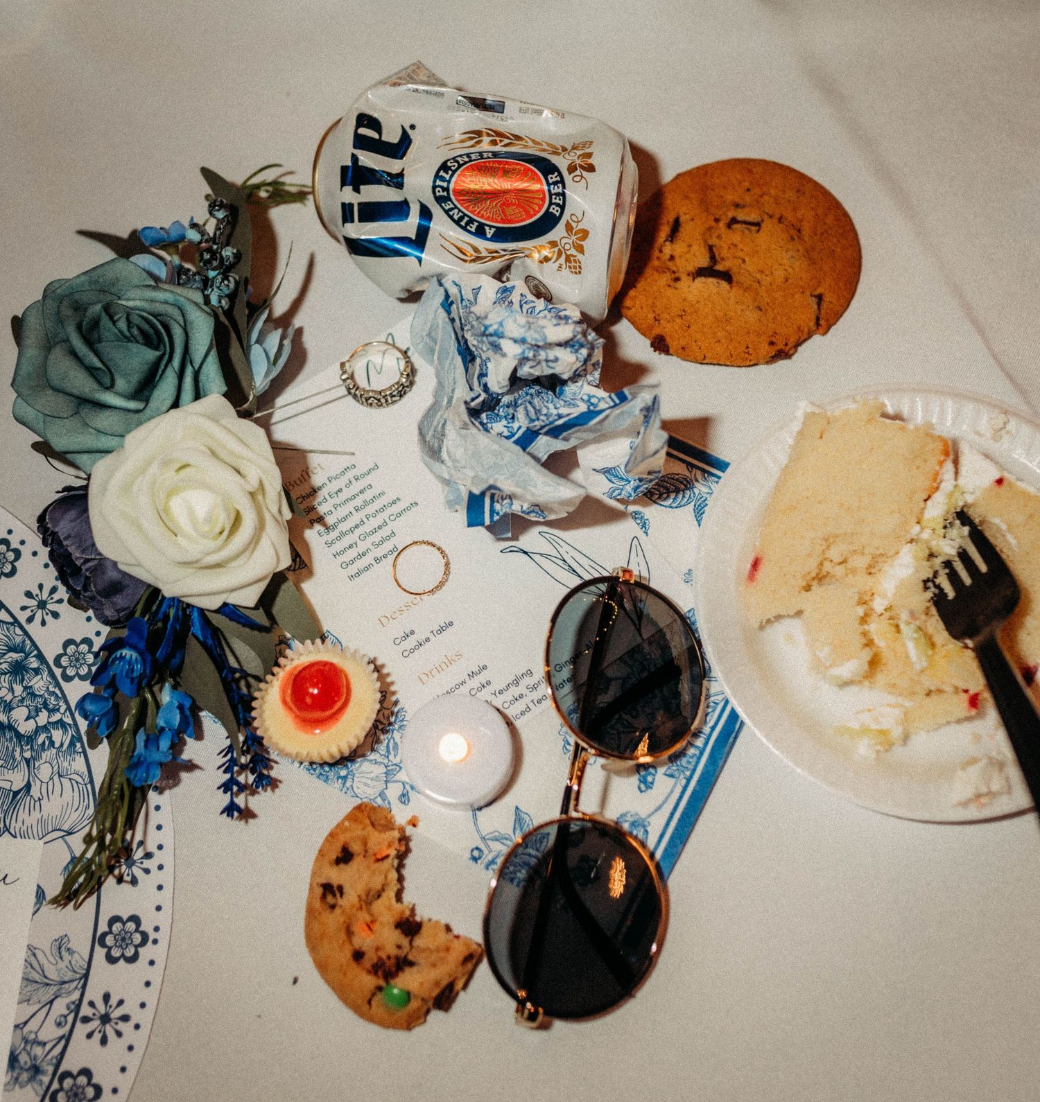 Wedding reception table with leftover desserts, blue decorations, and white roses.