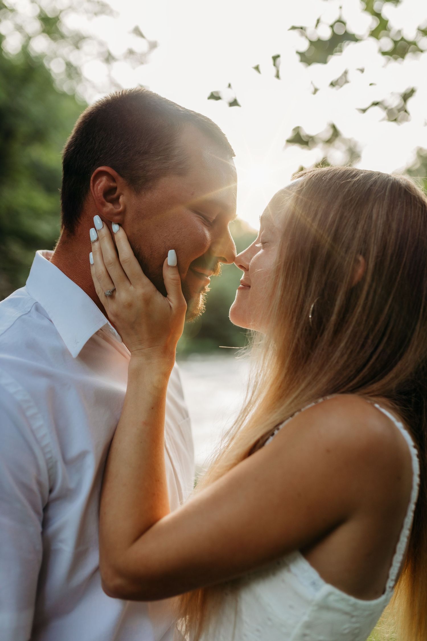Romantic couple sharing an intimate moment at sunset with sun flare in background.