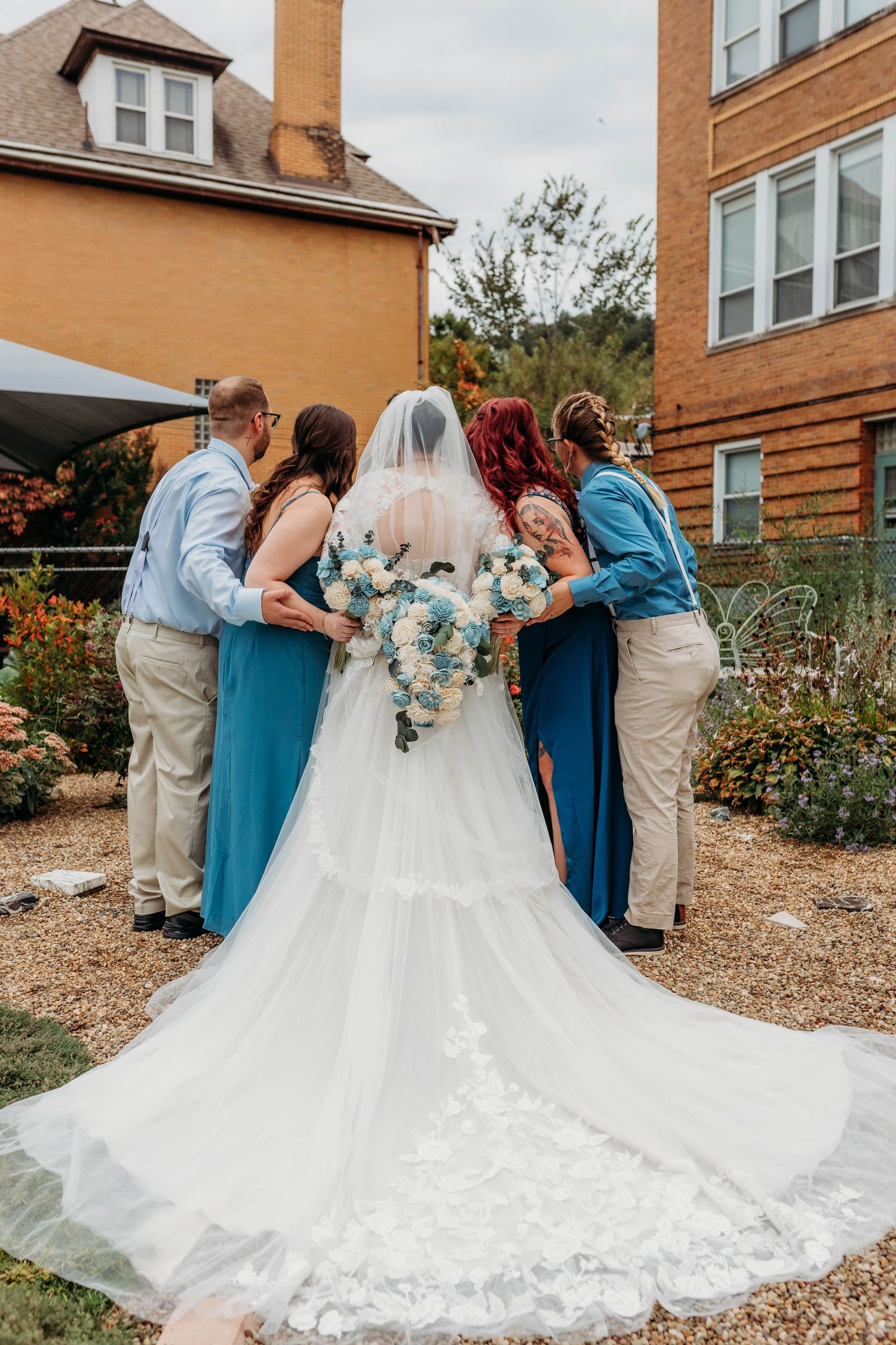 Wedding party in blue and neutral colors arranging the bride's dress train outdoors.
