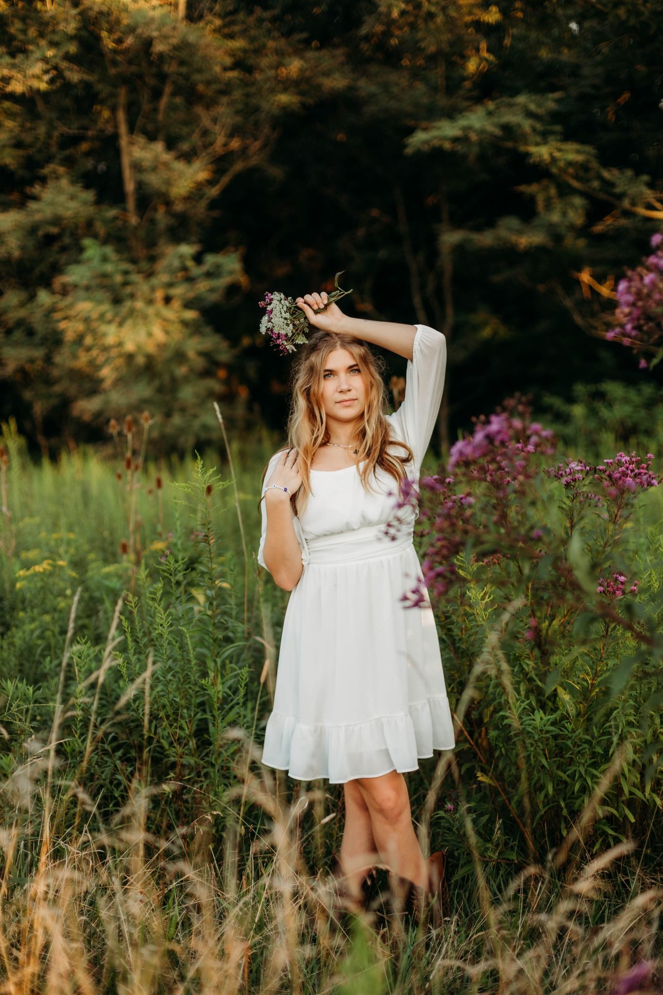 Woman in white dress poses elegantly among wildflowers at golden hour.