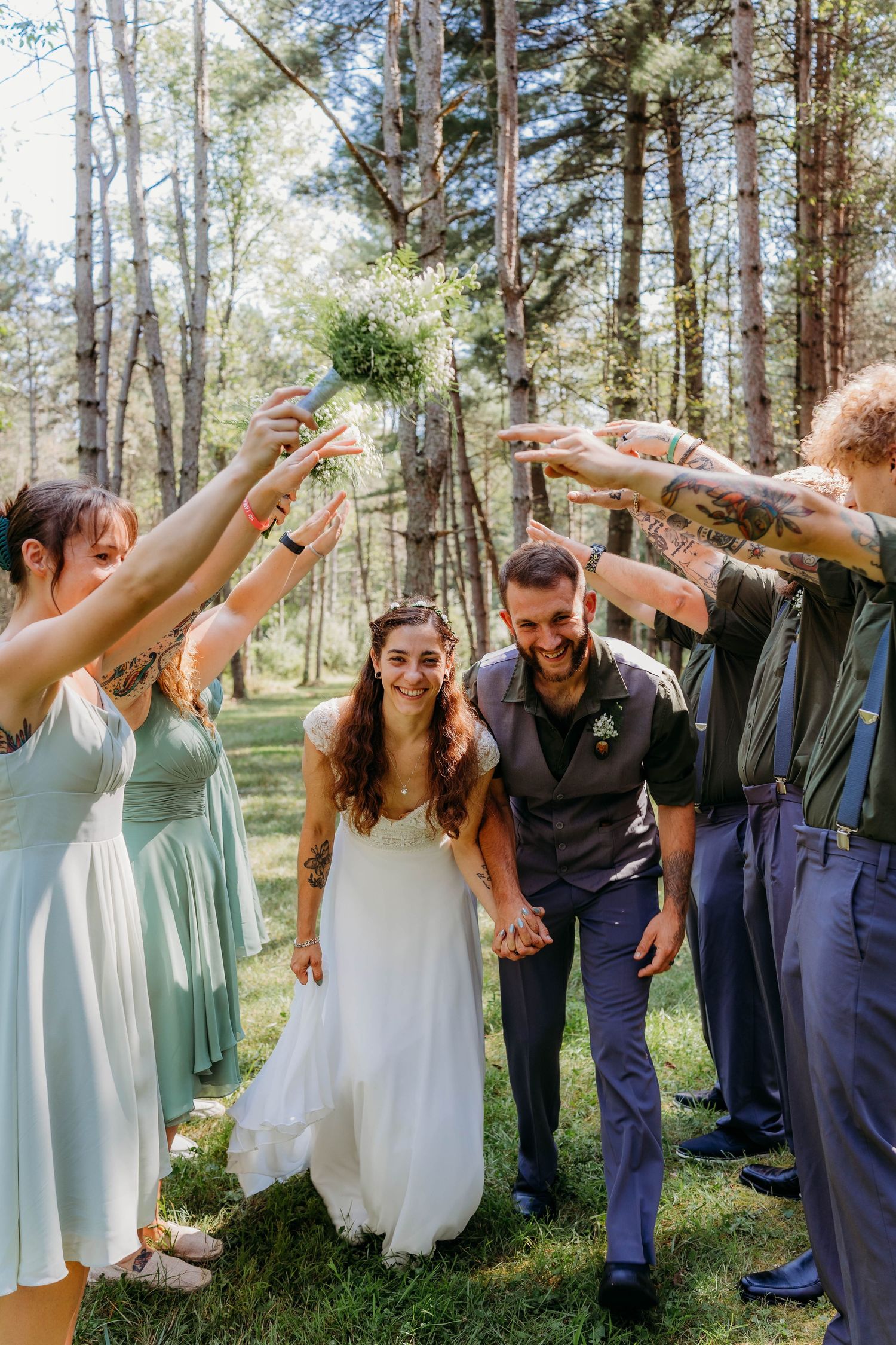 Wedding party in mint green dresses and navy suits posing playfully in a forest setting.