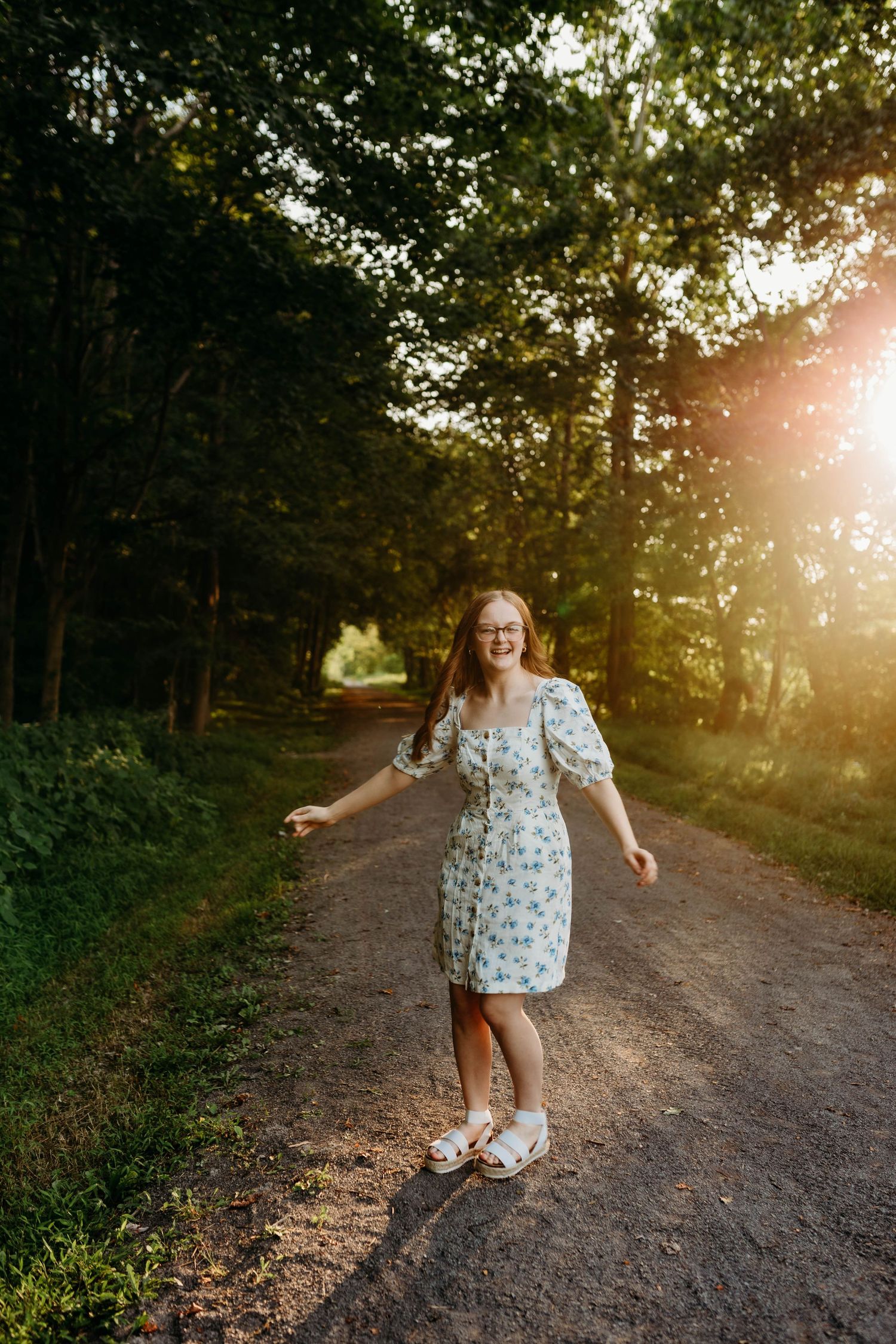 Person in a floral dress twirls and dances on a dirt path at sunset.