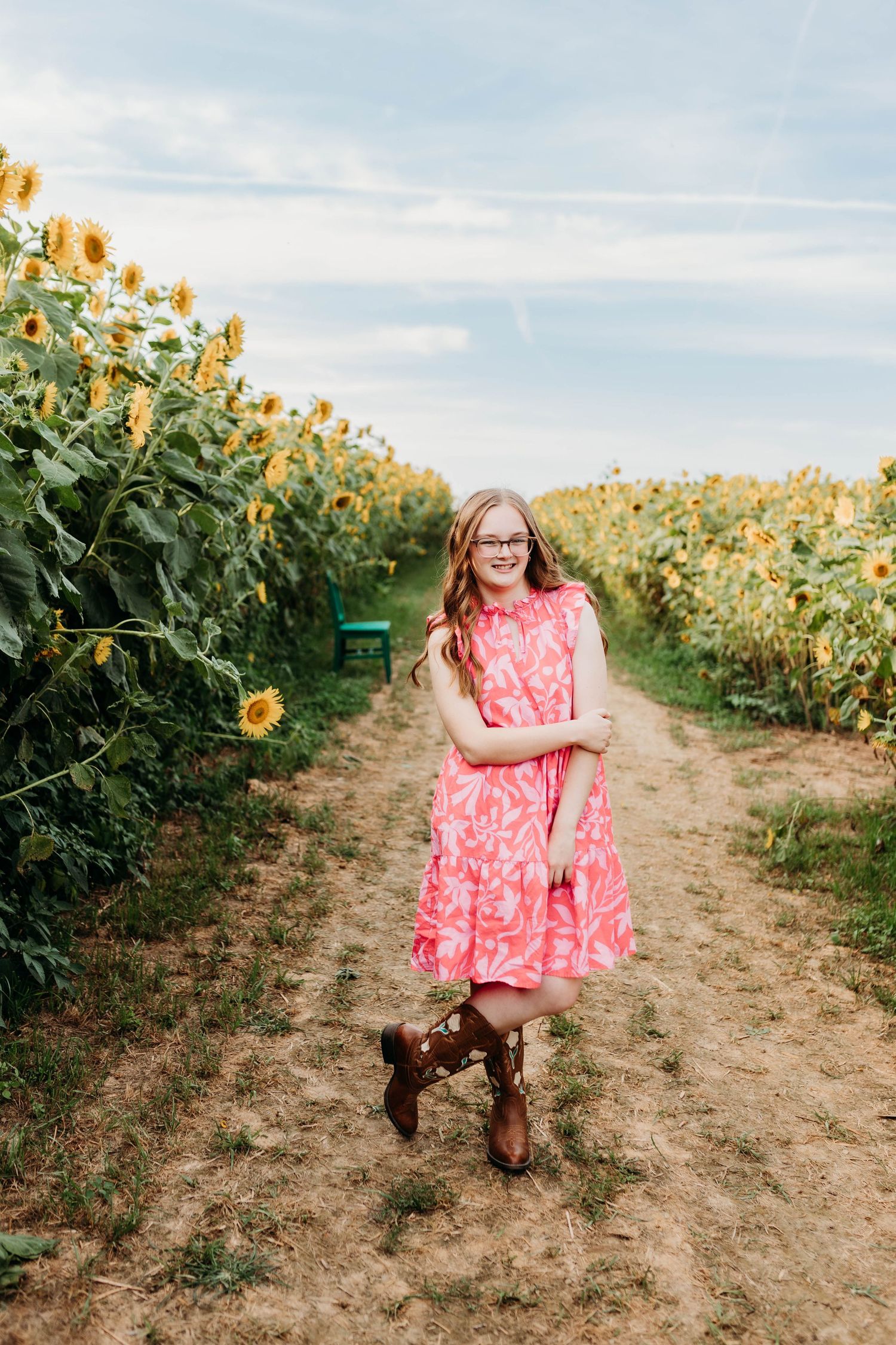 Person in a coral dress poses playfully in a field of tall sunflowers.