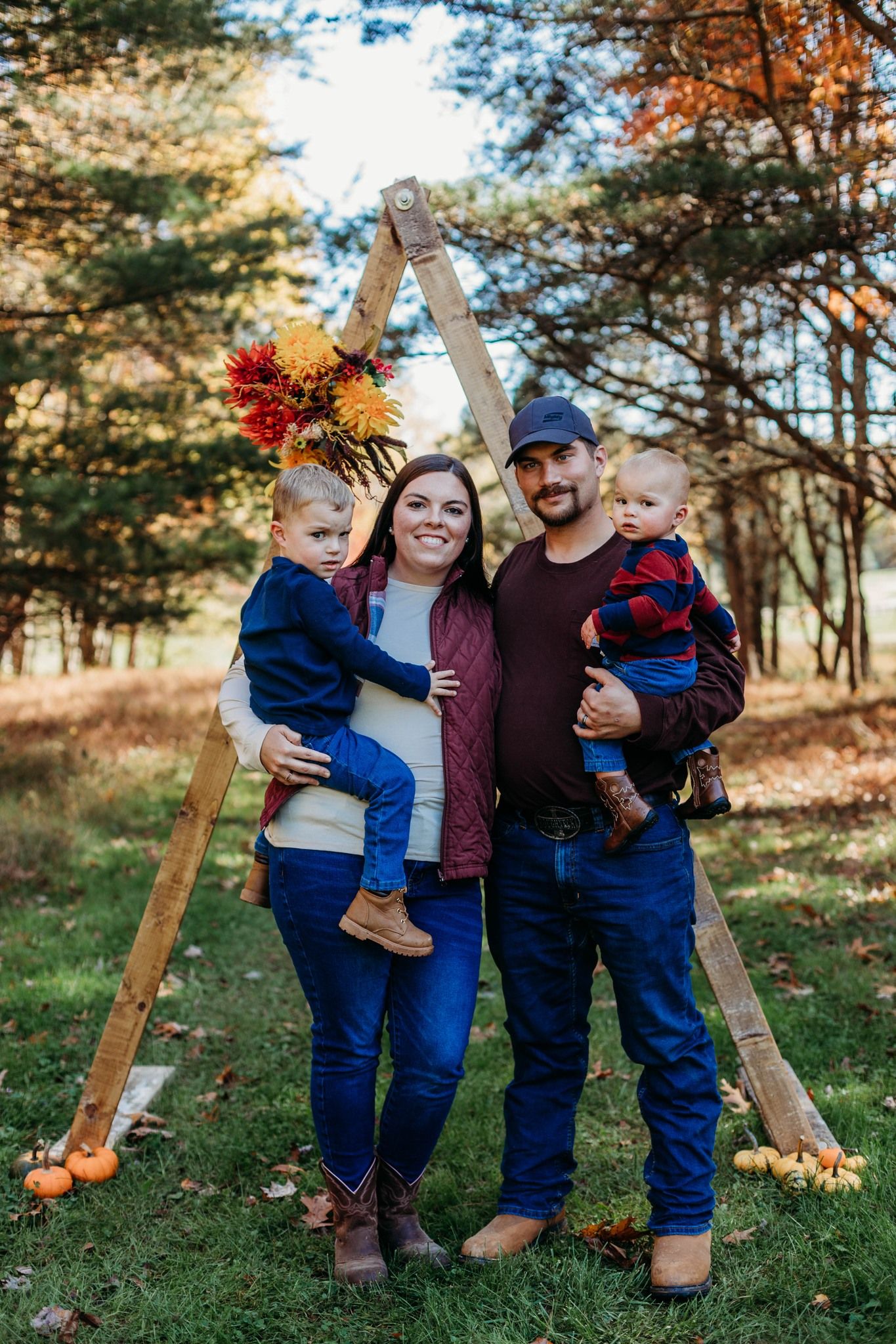 Family autumn portrait with wooden A-frame decorated with fall flowers in forest setting.
