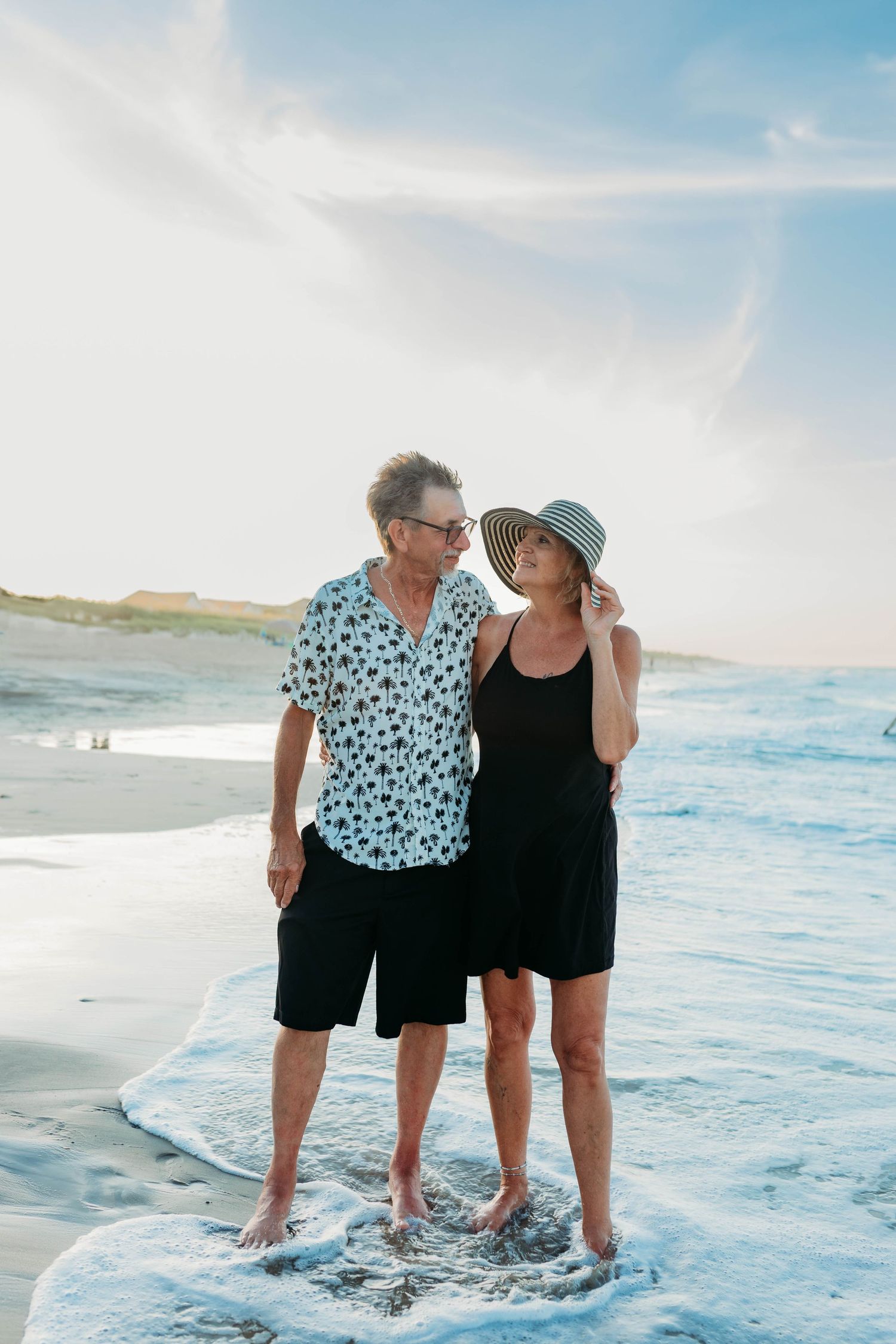Two people in casual summer attire playing in the ocean waves at the beach.