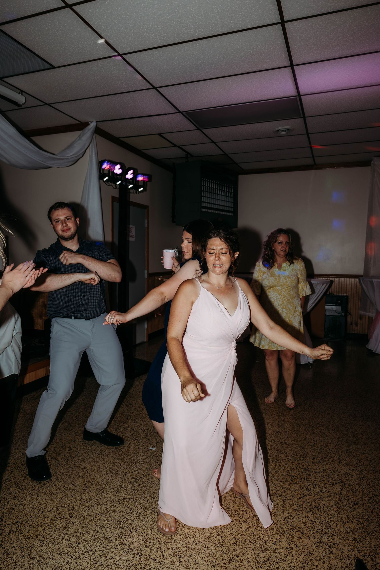 Guests dancing joyfully at a wedding reception, with a woman in a pink gown taking center stage on the dance floor.