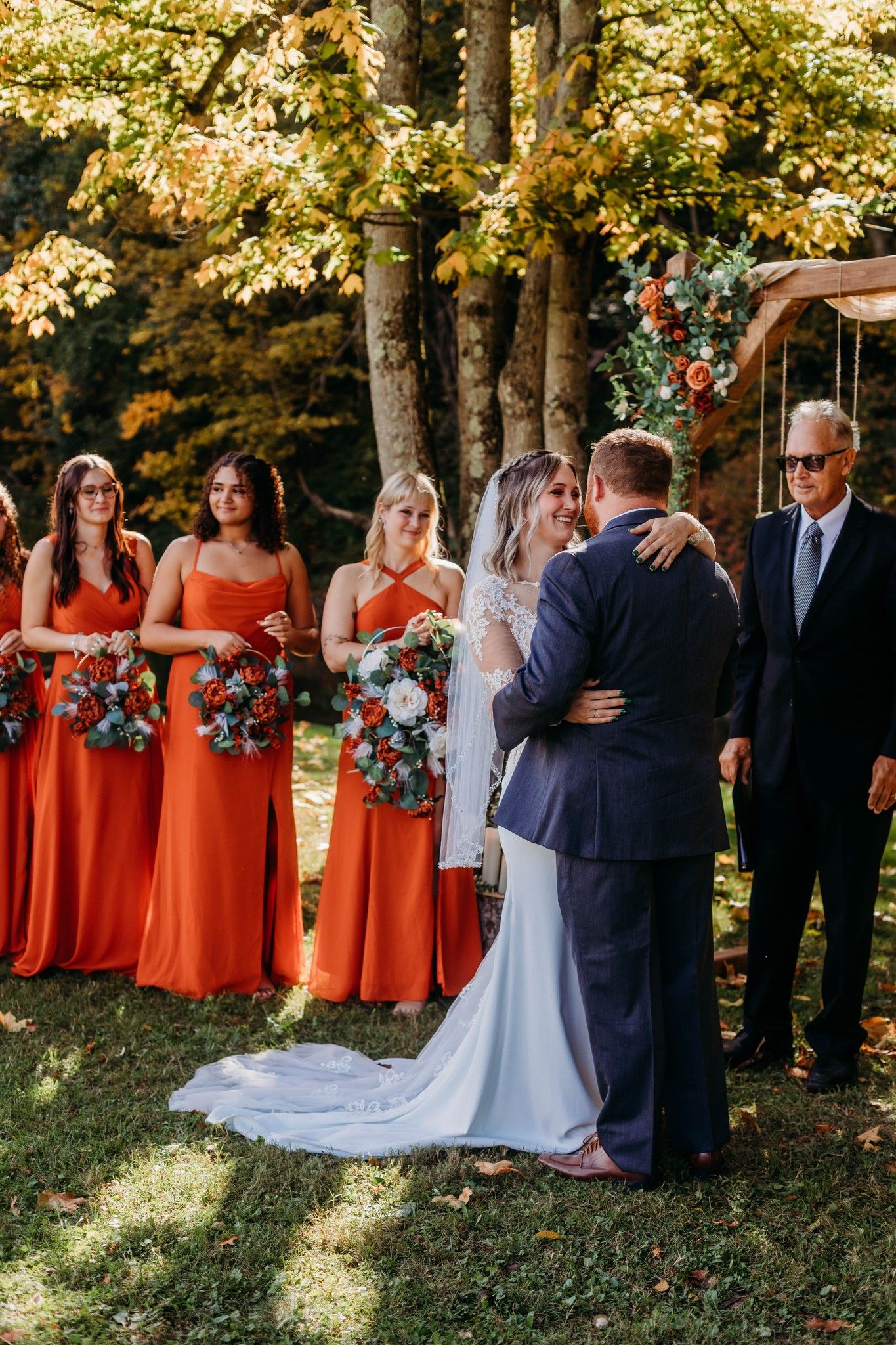 Wedding ceremony with bridesmaids in coral dresses watching couple's first kiss.