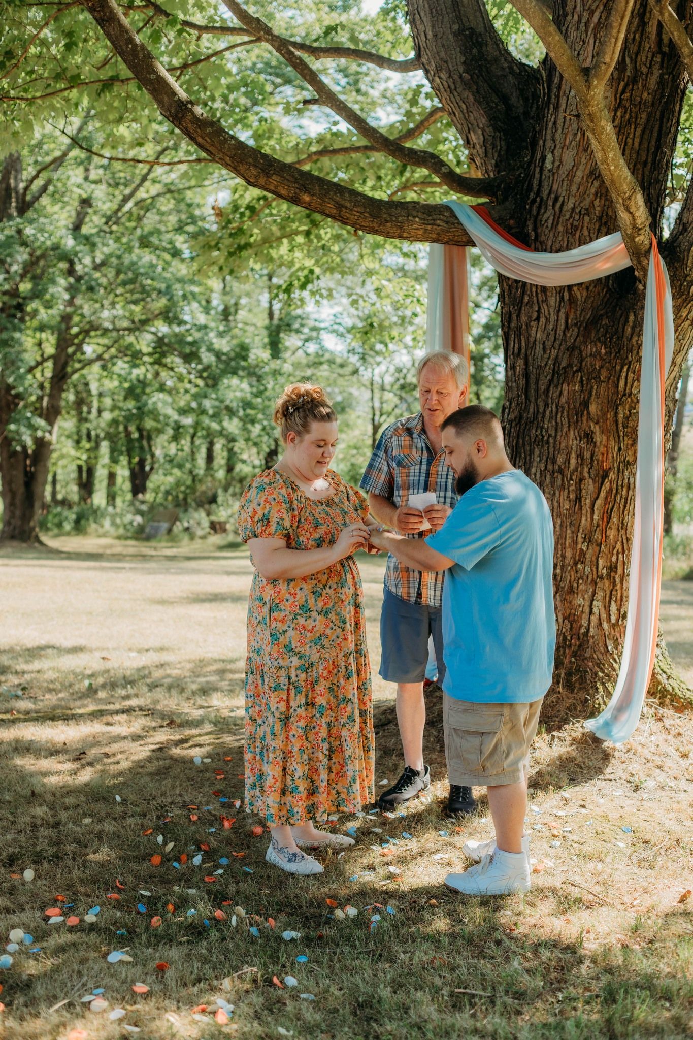Outdoor summer ceremony under tree decorated with light blue fabric draping.
