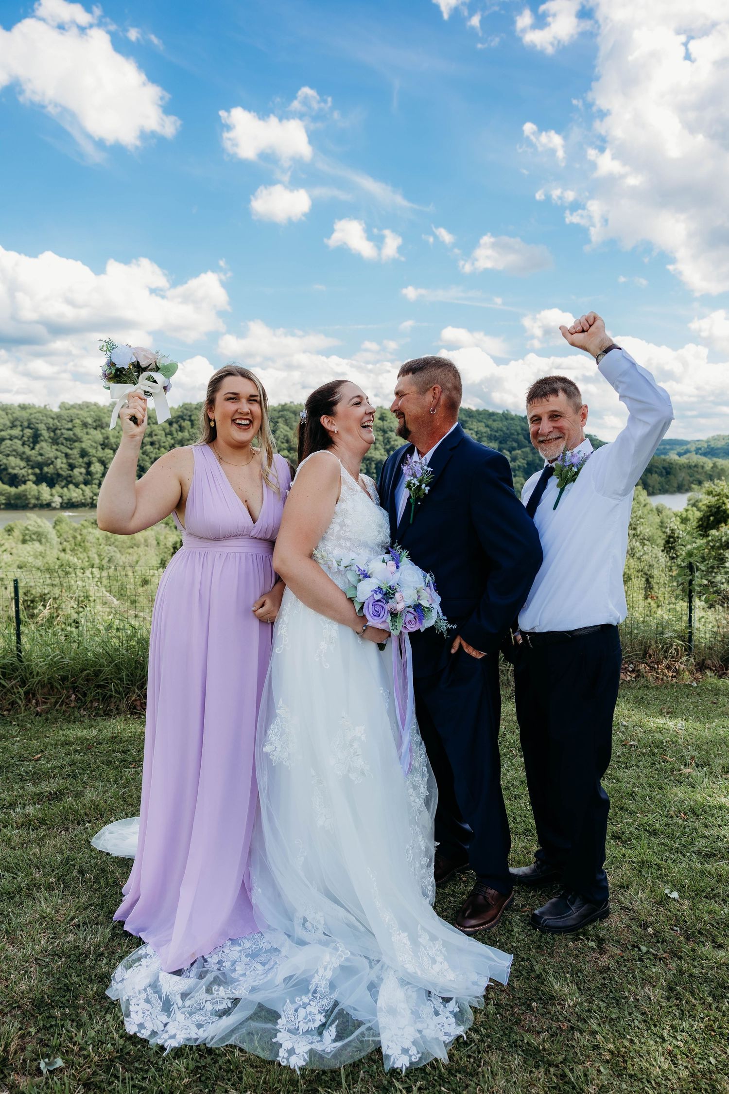 Bride in white gown with bridesmaids and groomsmen celebrating outdoors under blue sky at a vineyard wedding.
