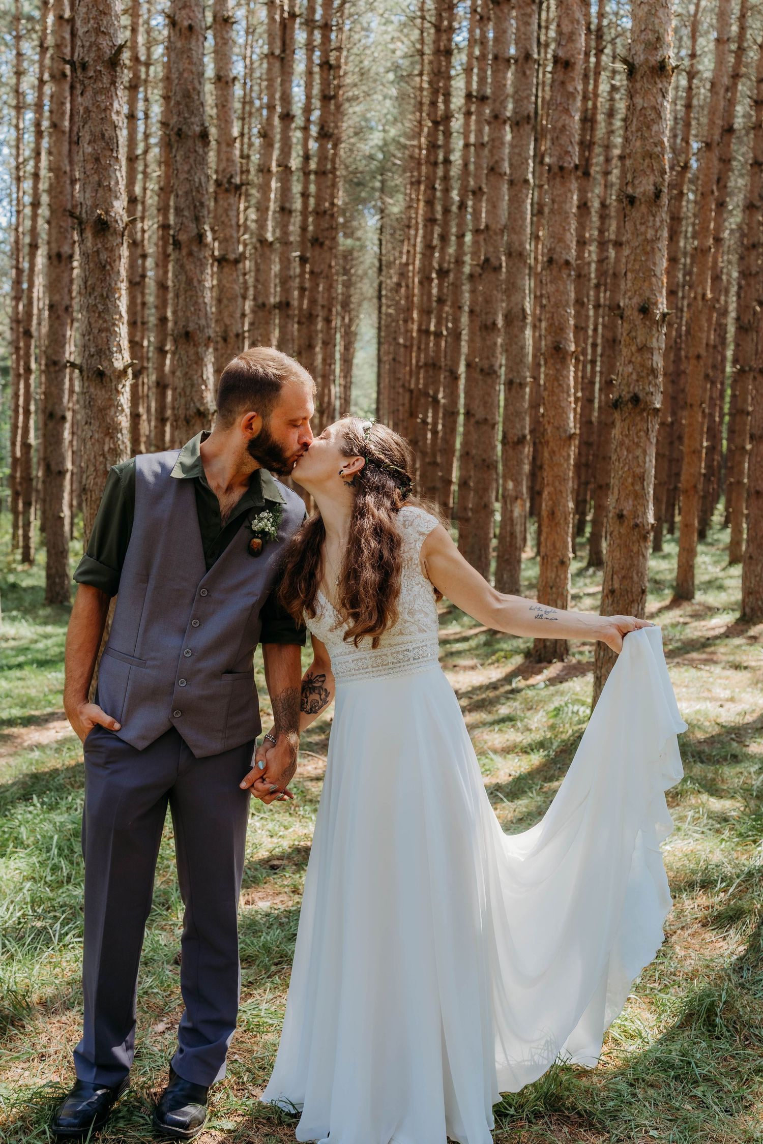 Couple in wedding attire sharing romantic moments among tall pine trees in a forest.