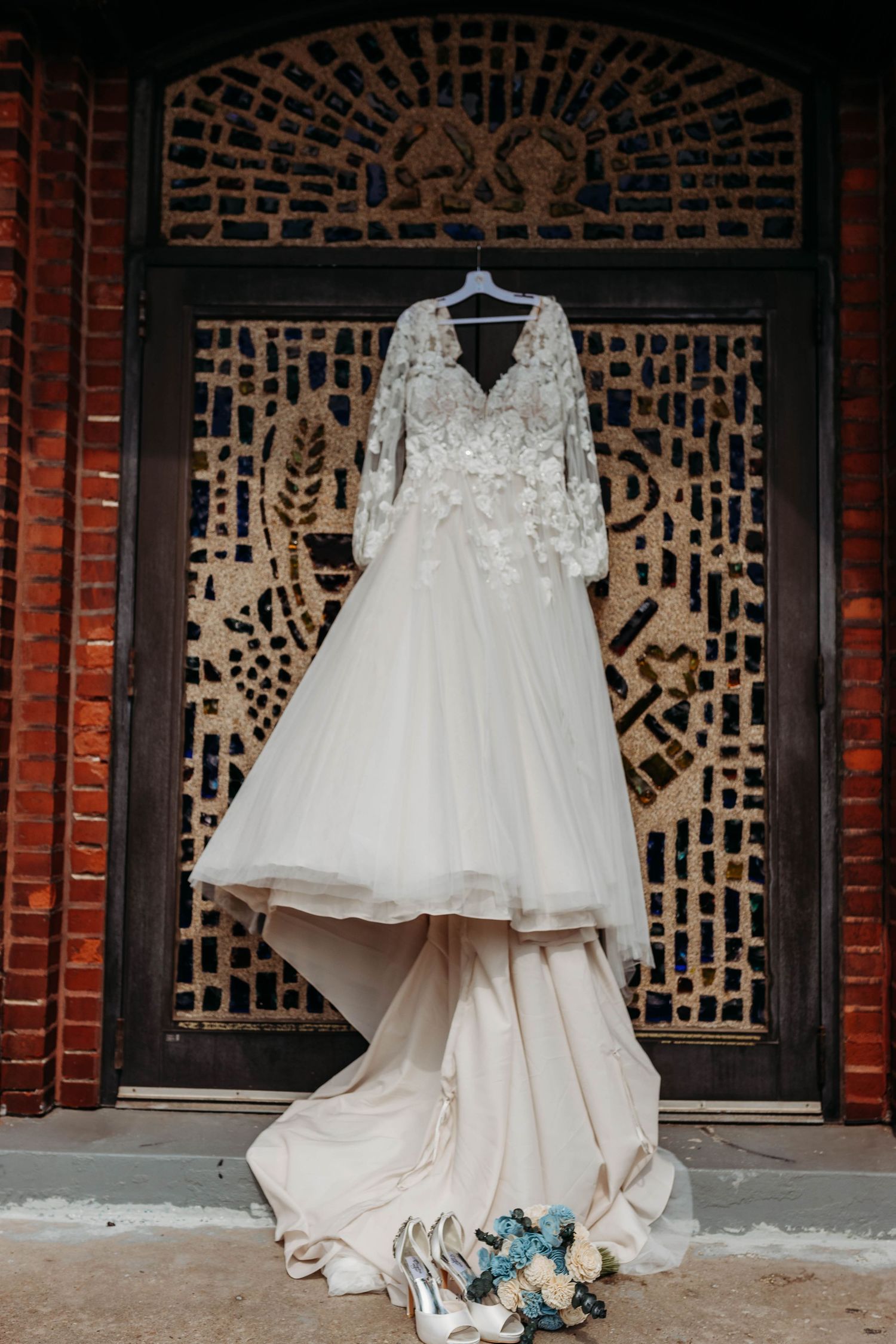 White lace wedding dress displayed against a decorative brick wall pattern.
