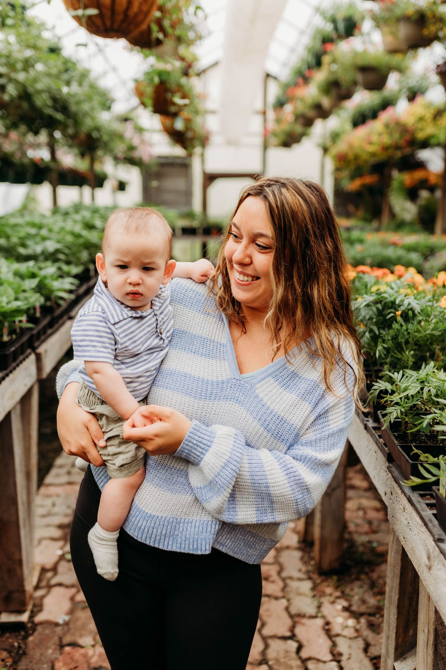 Parent and baby enjoying time together in a greenhouse filled with colorful flowers.