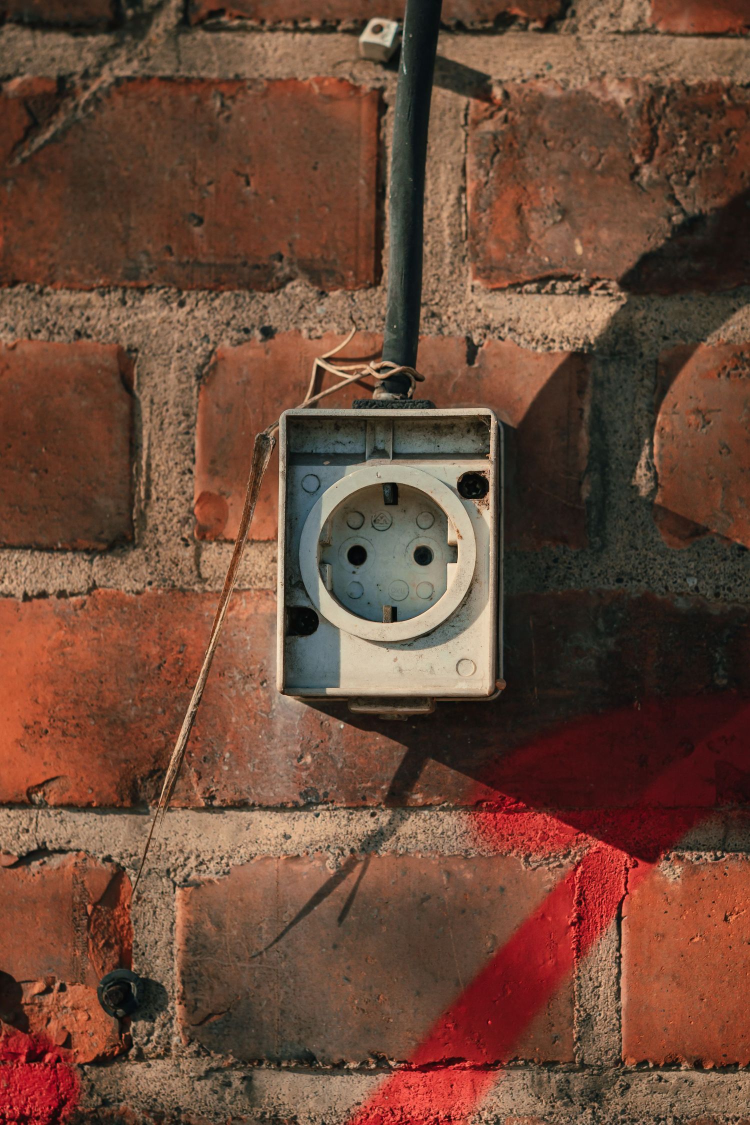 A single electrical outlet embedded in a textured brick wall, blending into the rough surface.