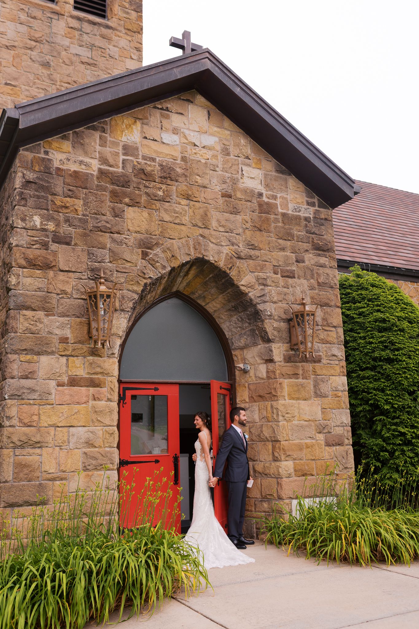 bride and groom holding hands on opposite sides of red door at stone church in butler, pa for their private touch and vow reading