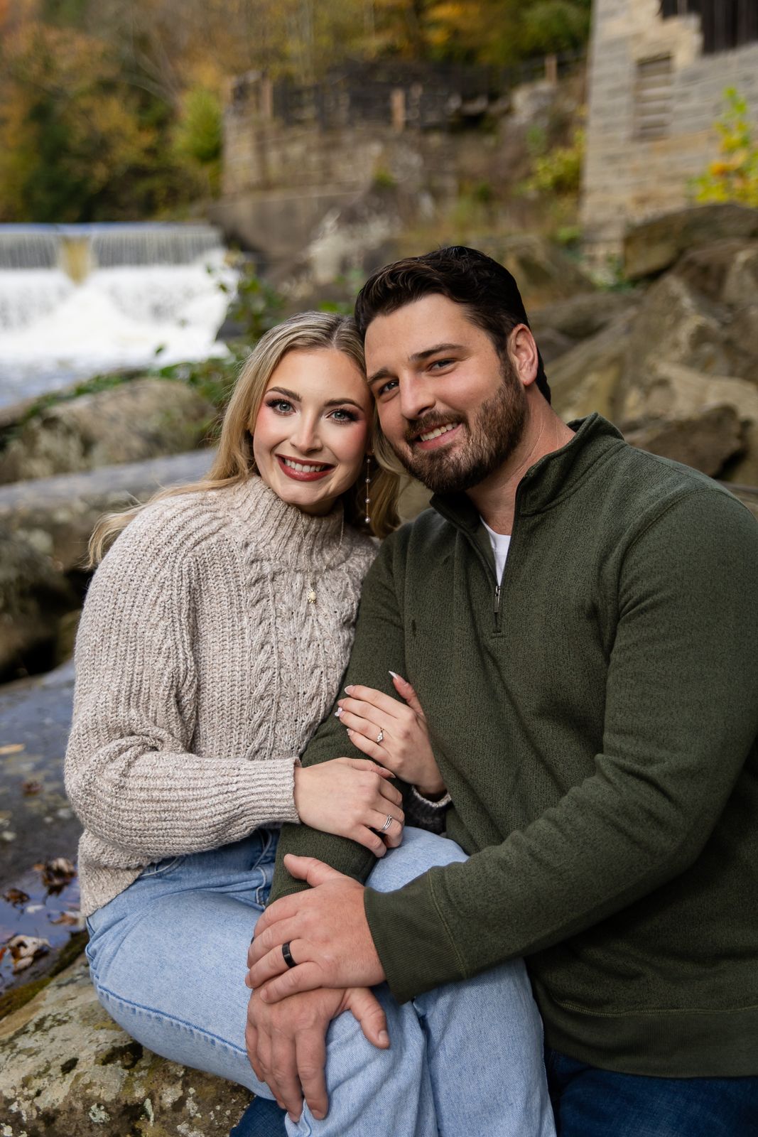 man and woman smiling and hugging during engagement photos with waterfall behind them